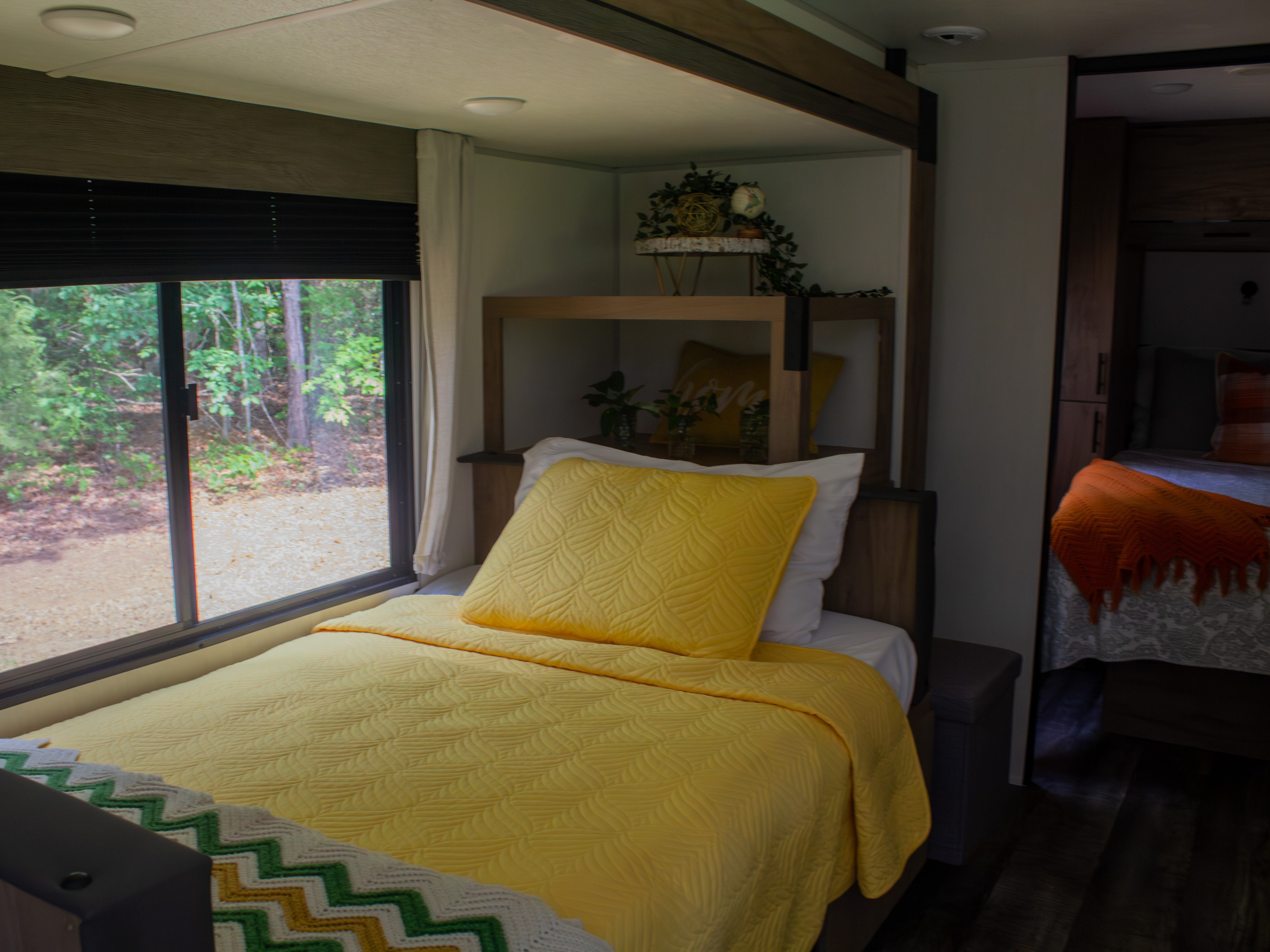 Relax in this cozy RV rental bedroom. Features a bright yellow bed, large window with nature views, and a comfy secondary bed.. Forest River Campsite Reserve 2025