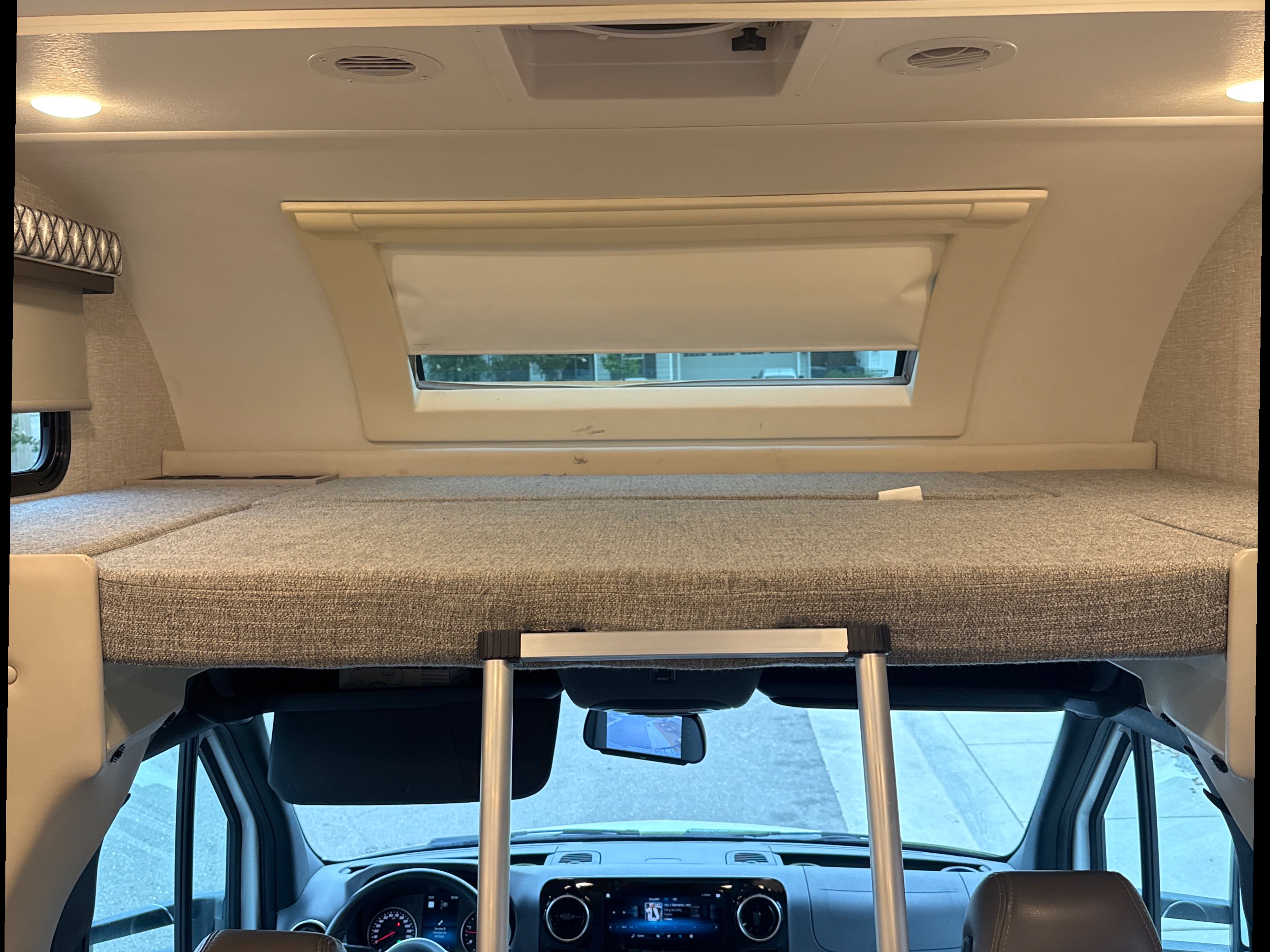 RV rental interior: Cab-over bunk bed with a ladder, overhead lights, and a view of the road from the driver's area.. Thor Quantum 2023