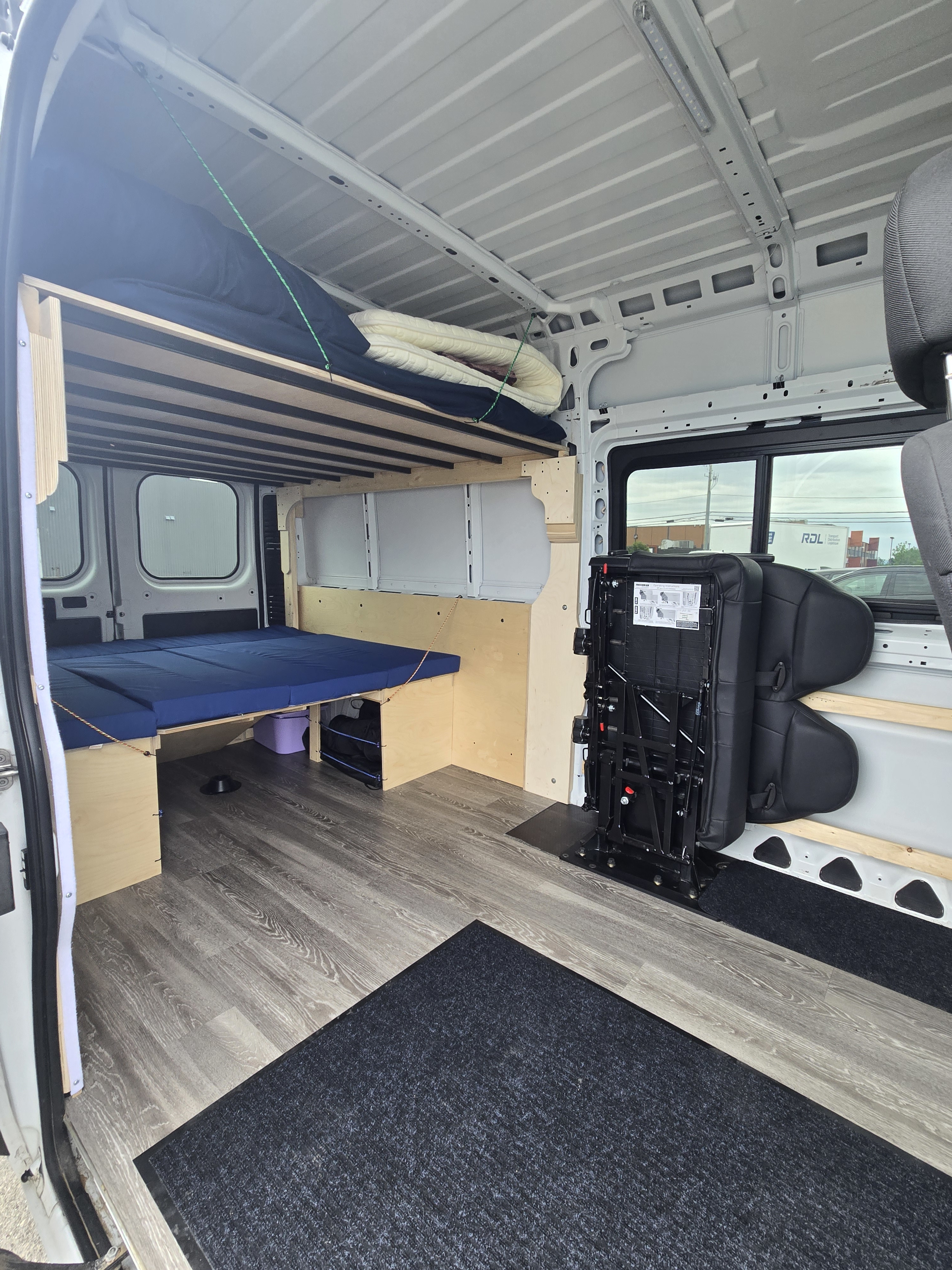 RV rental camper van interior featuring a lower bed with blue cushions, an upper bunk for storage/sleeping, and foldable seating.. Dodge Promaster 2500 2019