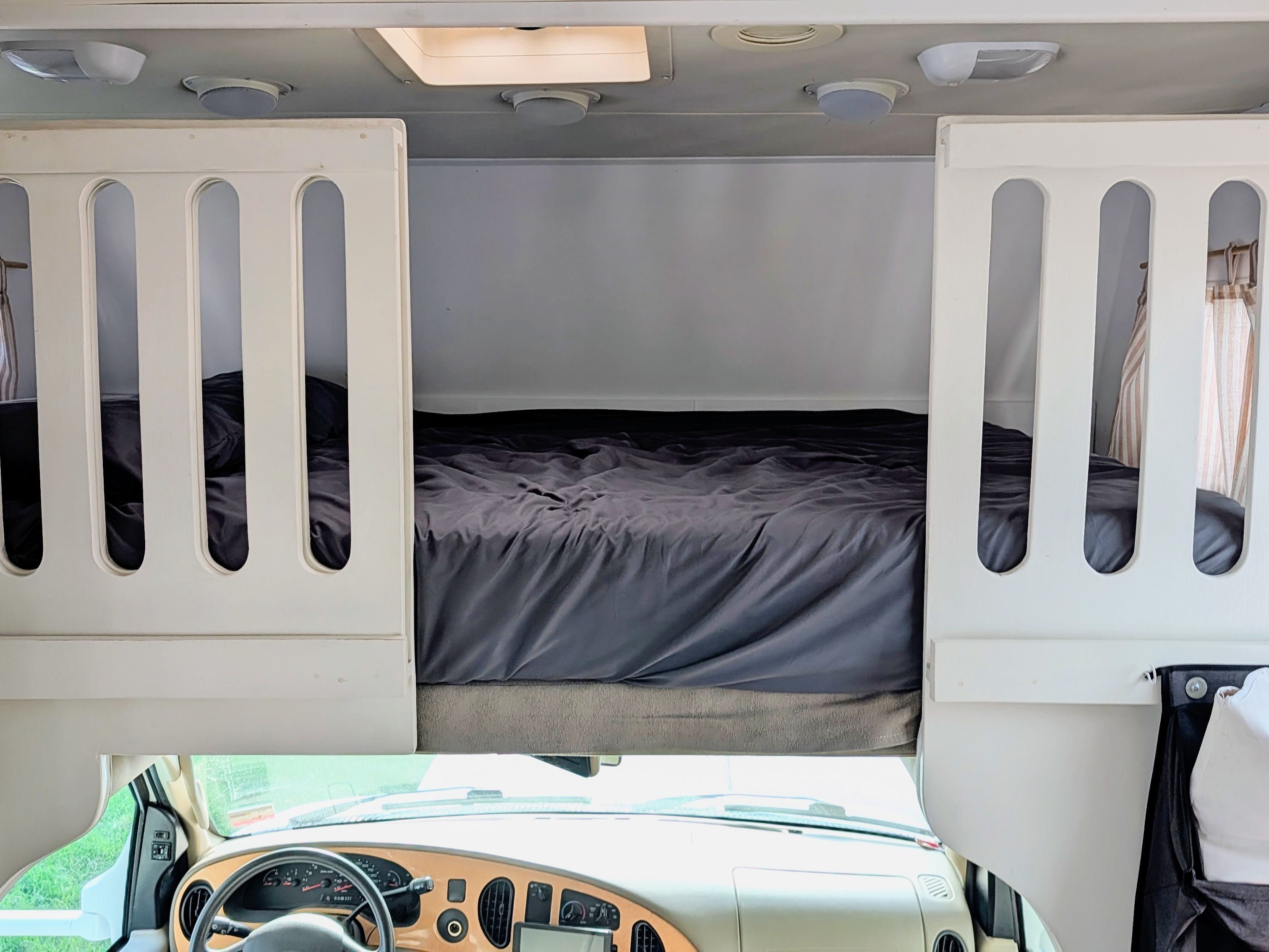 The over-cab bunk bed of an RV rental, featuring dark bedding and safety rails, positioned above the driver's dashboard.. Jayco Greyhawk 2007