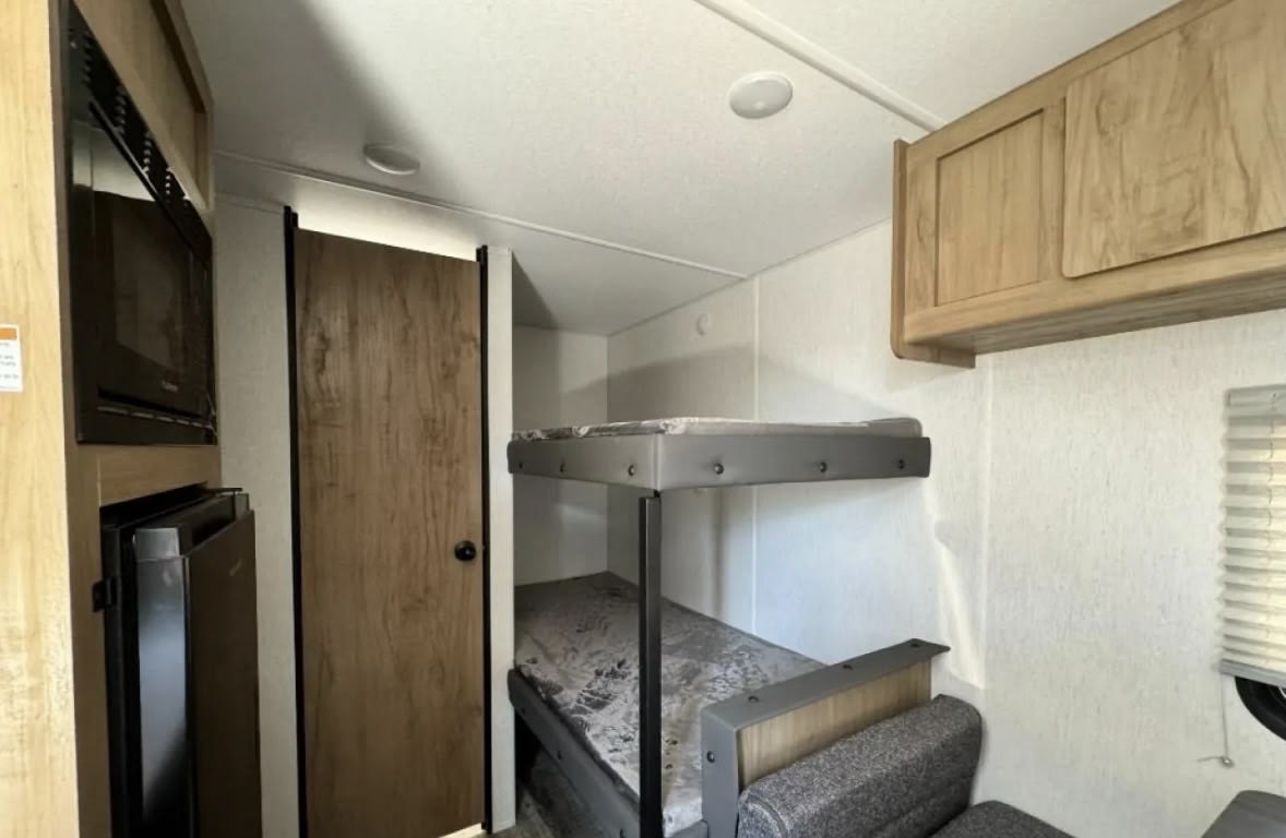 Cozy RV rental interior with stacked bunk beds, microwave, fridge, and wood cabinetry. Ideal for family adventures!. Forest River Cherokee Wolf Den 2024
