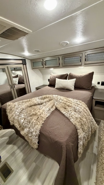 Inside this RV rental, a bedroom features a large bed, faux fur throw, ample overhead storage, and mirrored closet doors.. Coachman Chaparral 2022