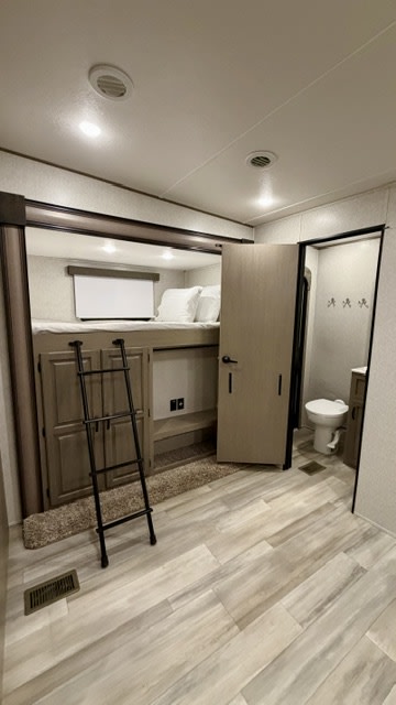 This rv rental features bunk beds with a ladder, a compact bathroom, and light wood-look flooring. Ideal for family travel.. Coachman Chaparral 2022