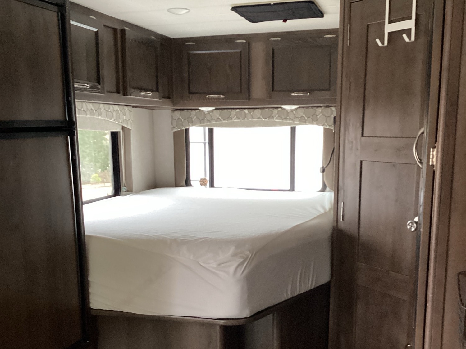 Step into comfort in this RV rental bedroom, featuring a neatly made bed, overhead storage, and bright windows.. Coachman Freelander 2019