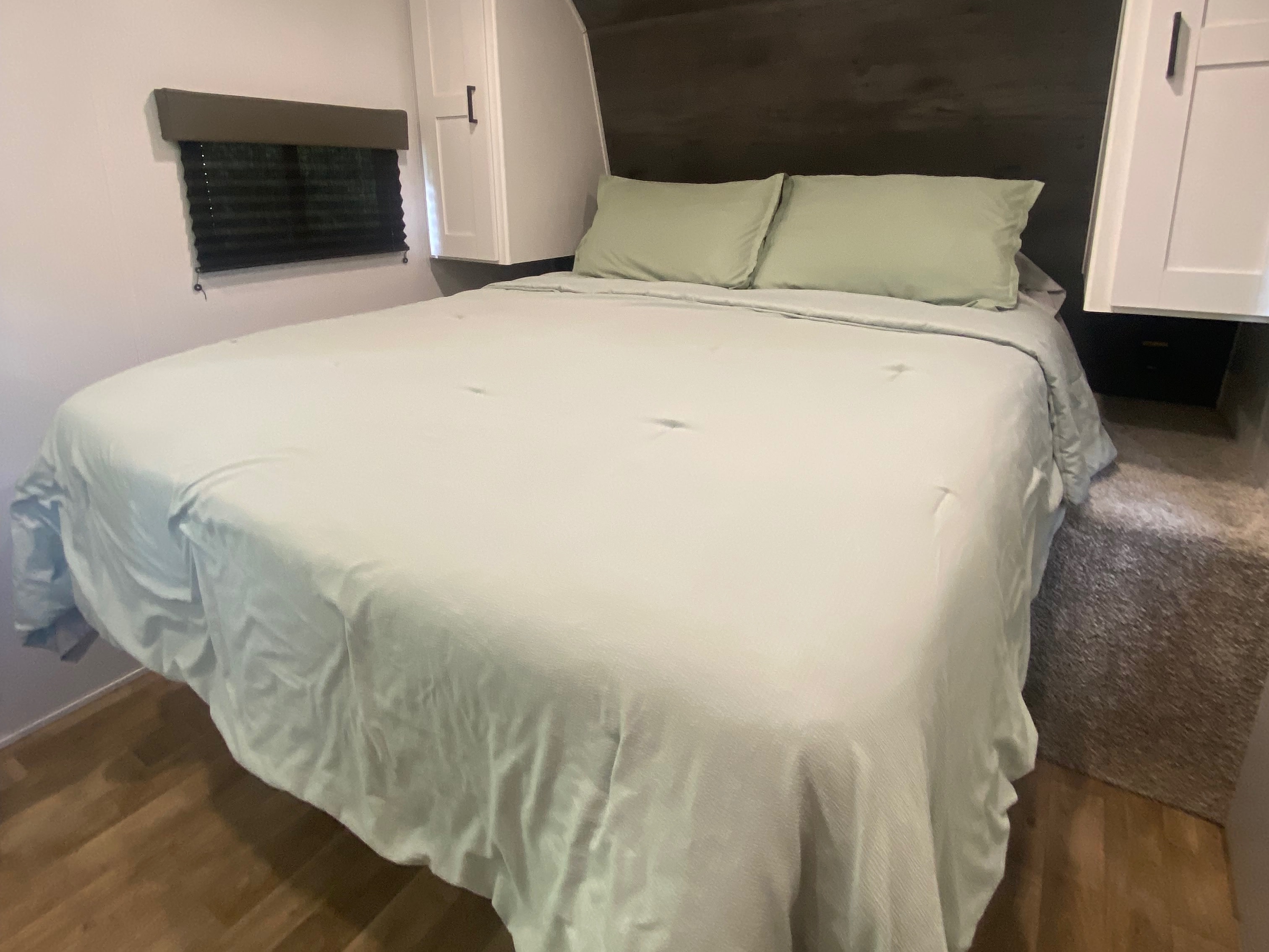 Inside an RV rental: A clean bedroom with a neatly made bed, light green pillows, and overhead cabinets.. Keystone RV Hideout 2022