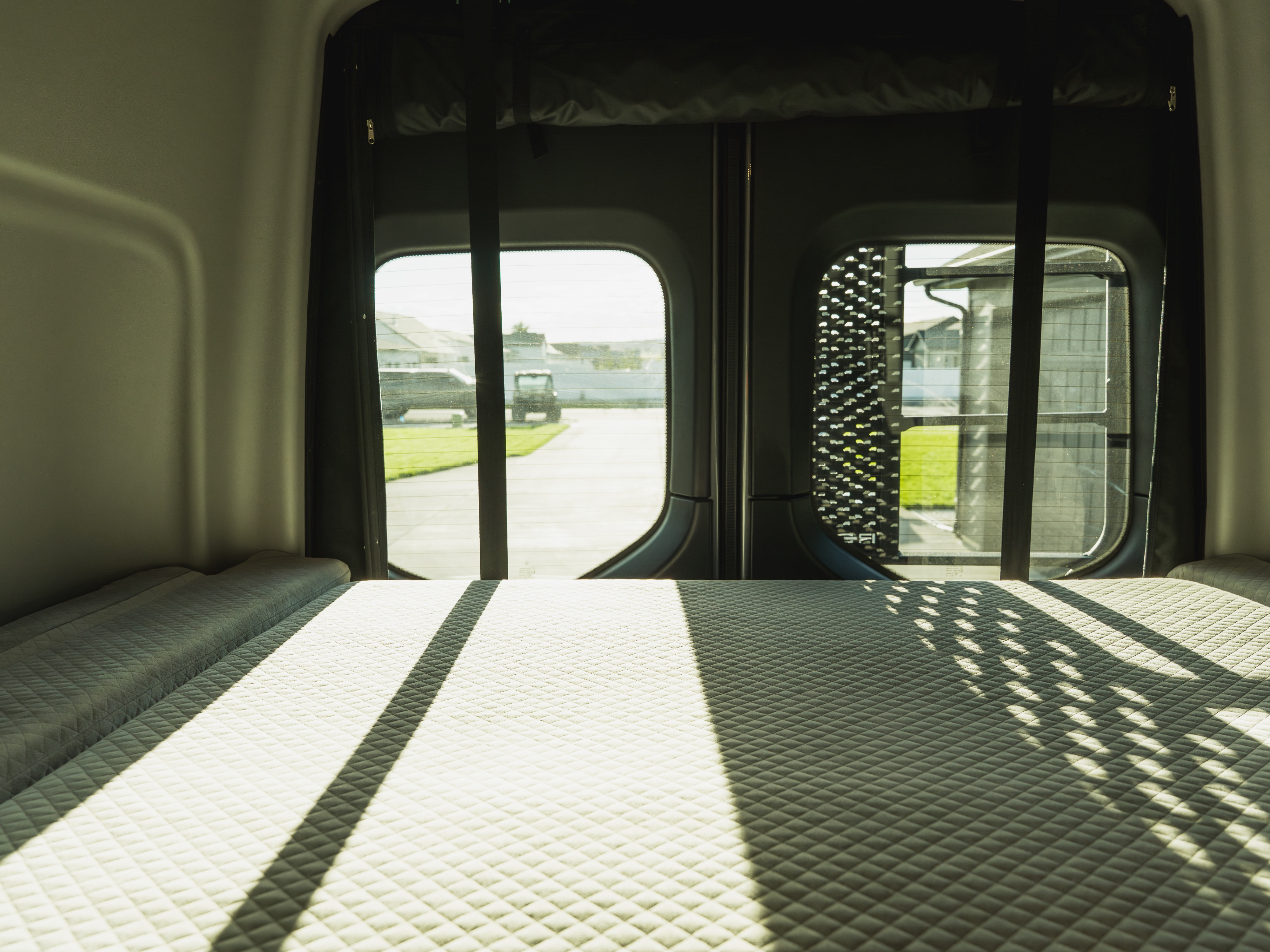 Comfortable quilted bed inside an rv rental, with sunlight streaming through the rear windows showcasing a view of the outside.. Winnebago Revel 2025
