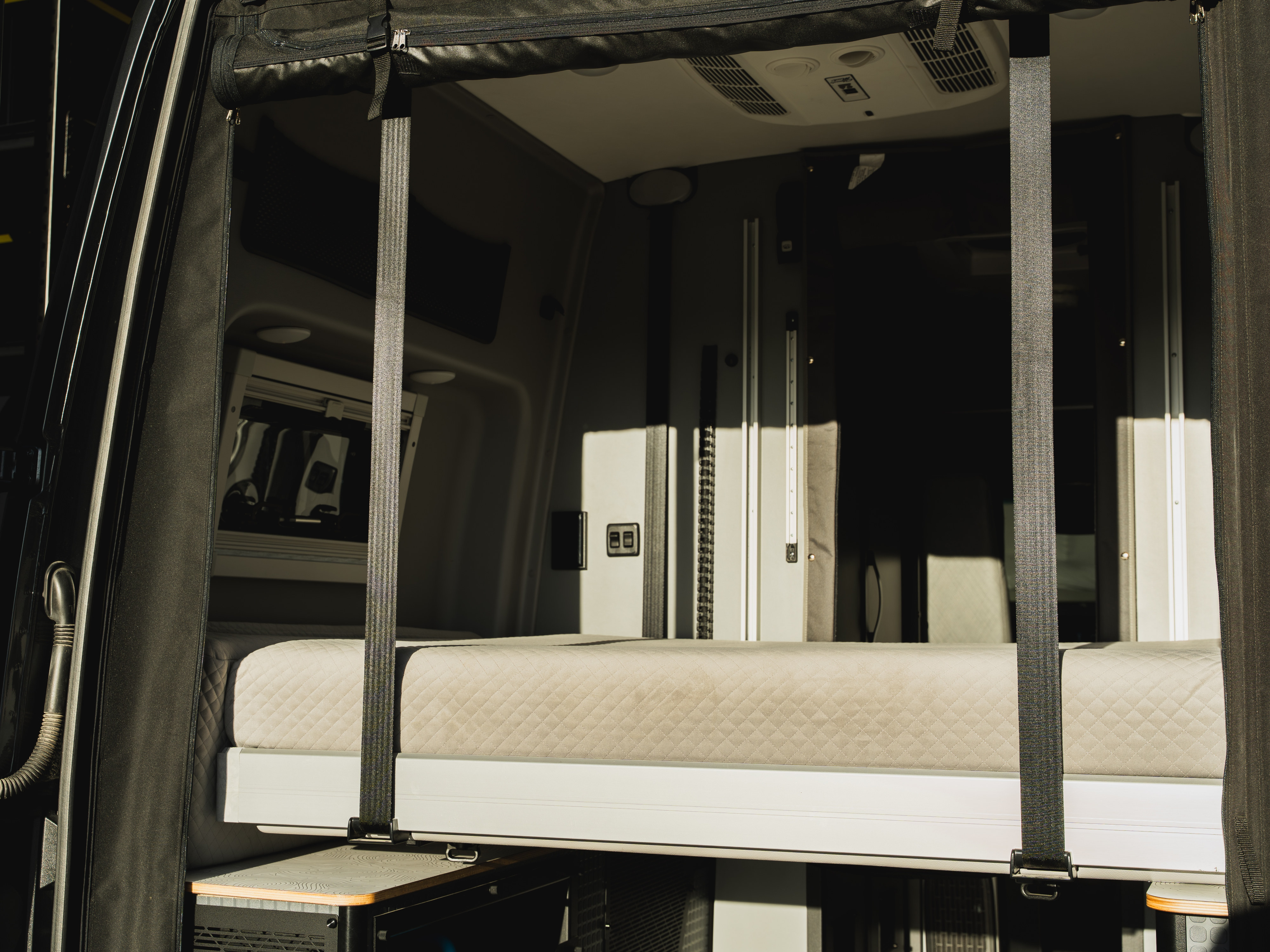 RV rental camper van interior featuring a quilted bed with straps, overhead vents, and integrated storage, ready for adventure.. Winnebago Revel 2025