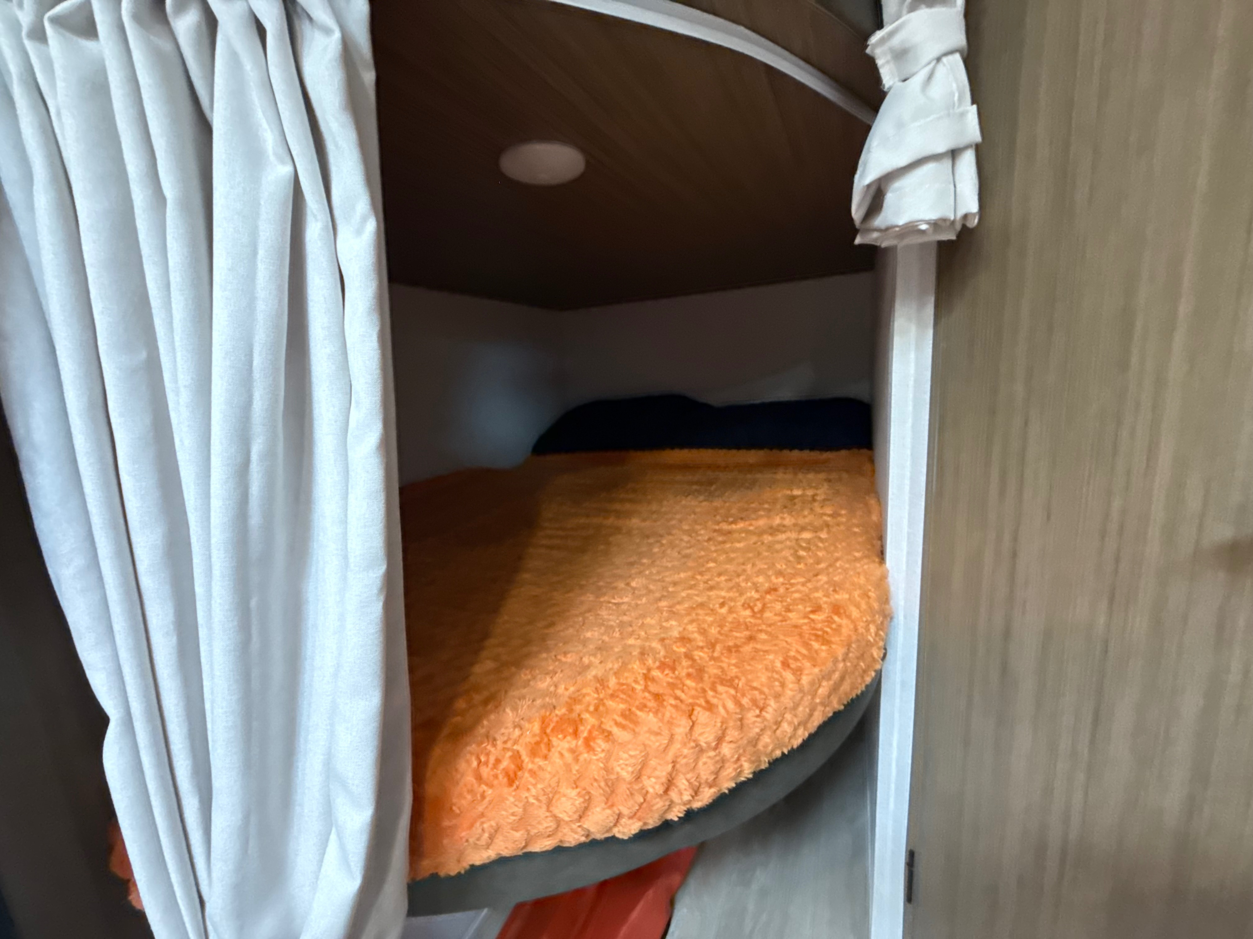 An RV rental's cozy bunk bed, featuring an orange blanket and internal light, partially framed by white privacy curtains.. Forest River Salem 2026