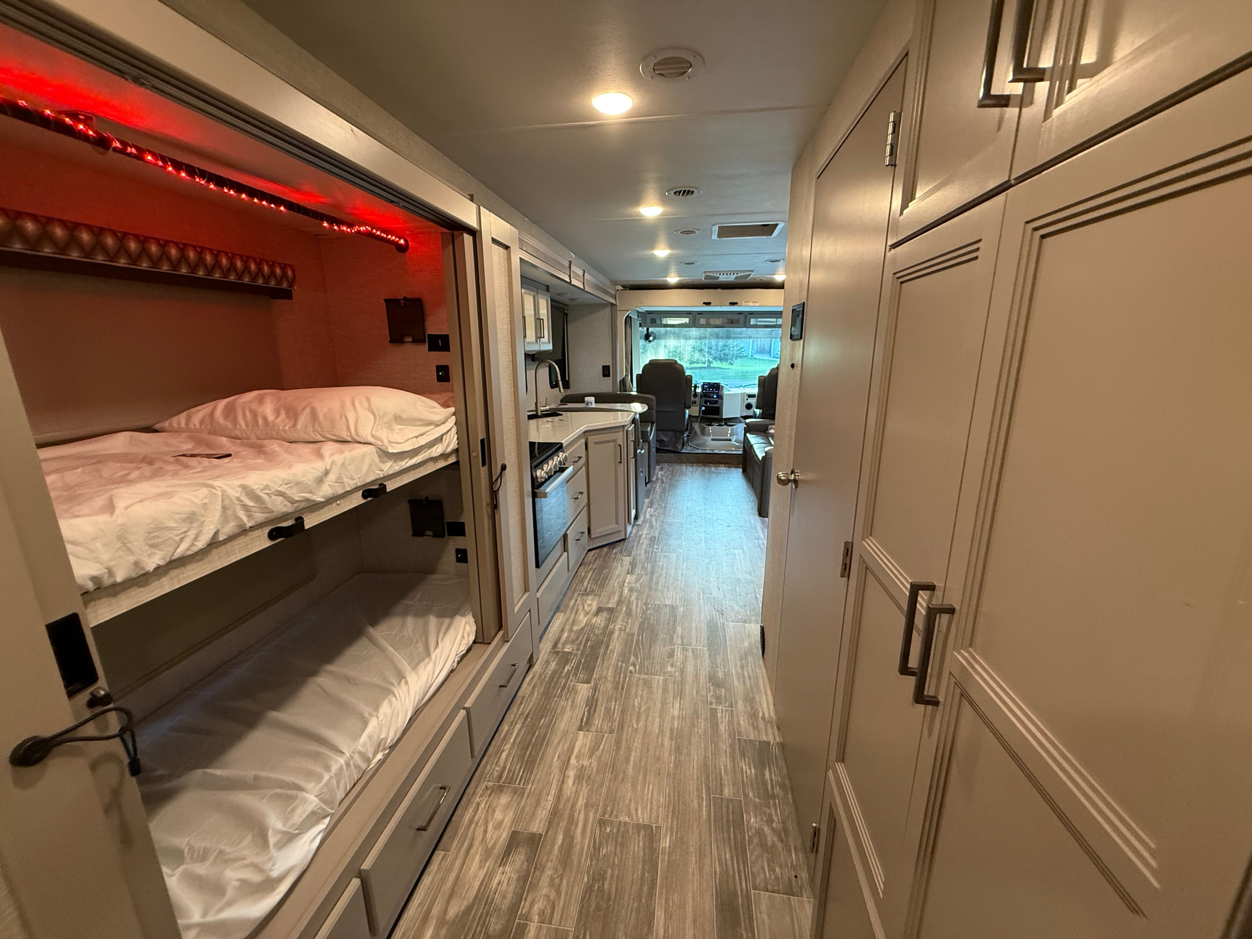 RV rental interior showcasing bunk beds with red LEDs, a modern kitchen, and the driver's cabin view ahead.. Thor Hurricane 2022