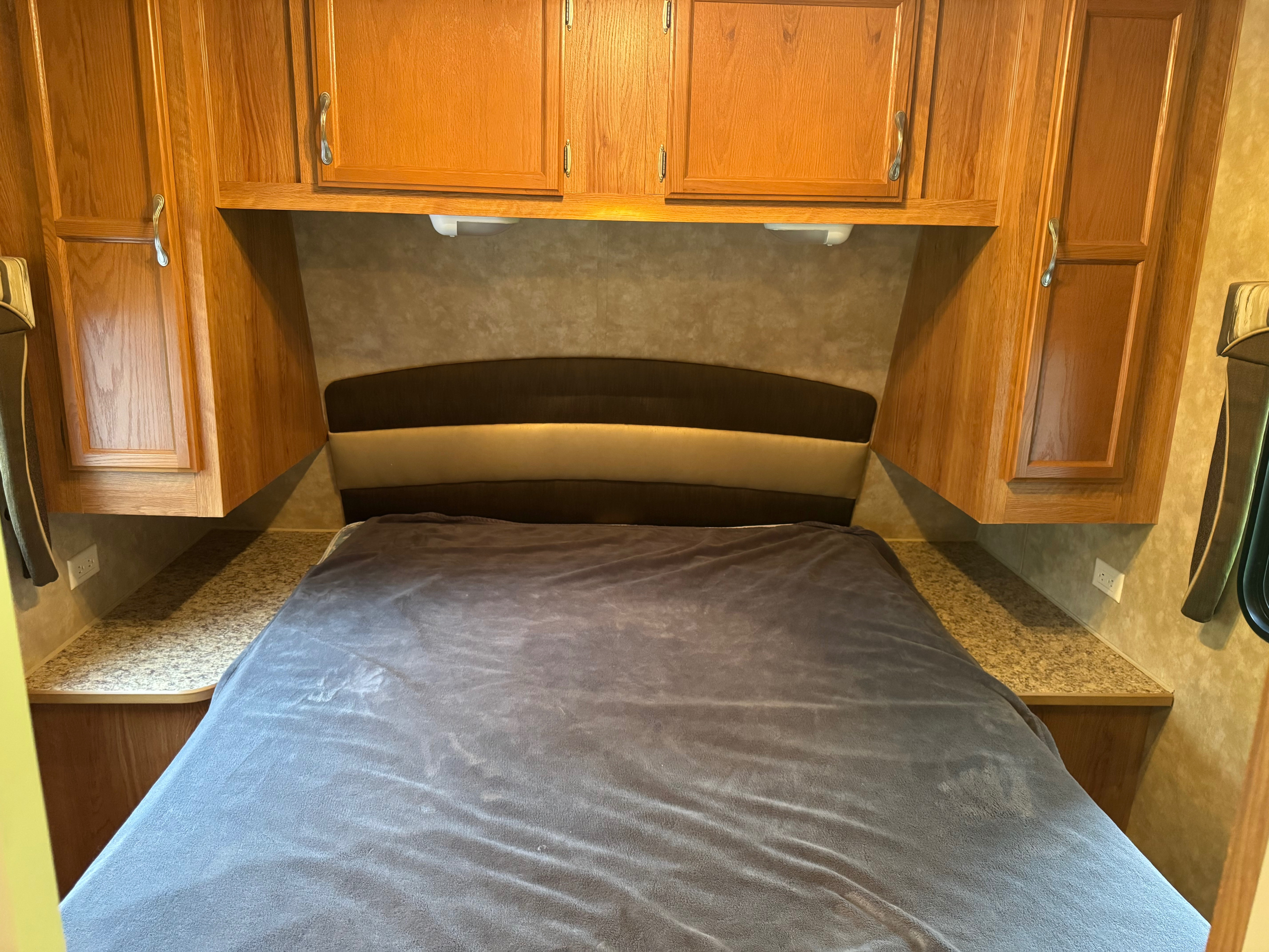 This RV rental bedroom features a neatly made bed, wood cabinetry above and on sides, and a padded headboard.. Jayco Jay Flight G2 2008