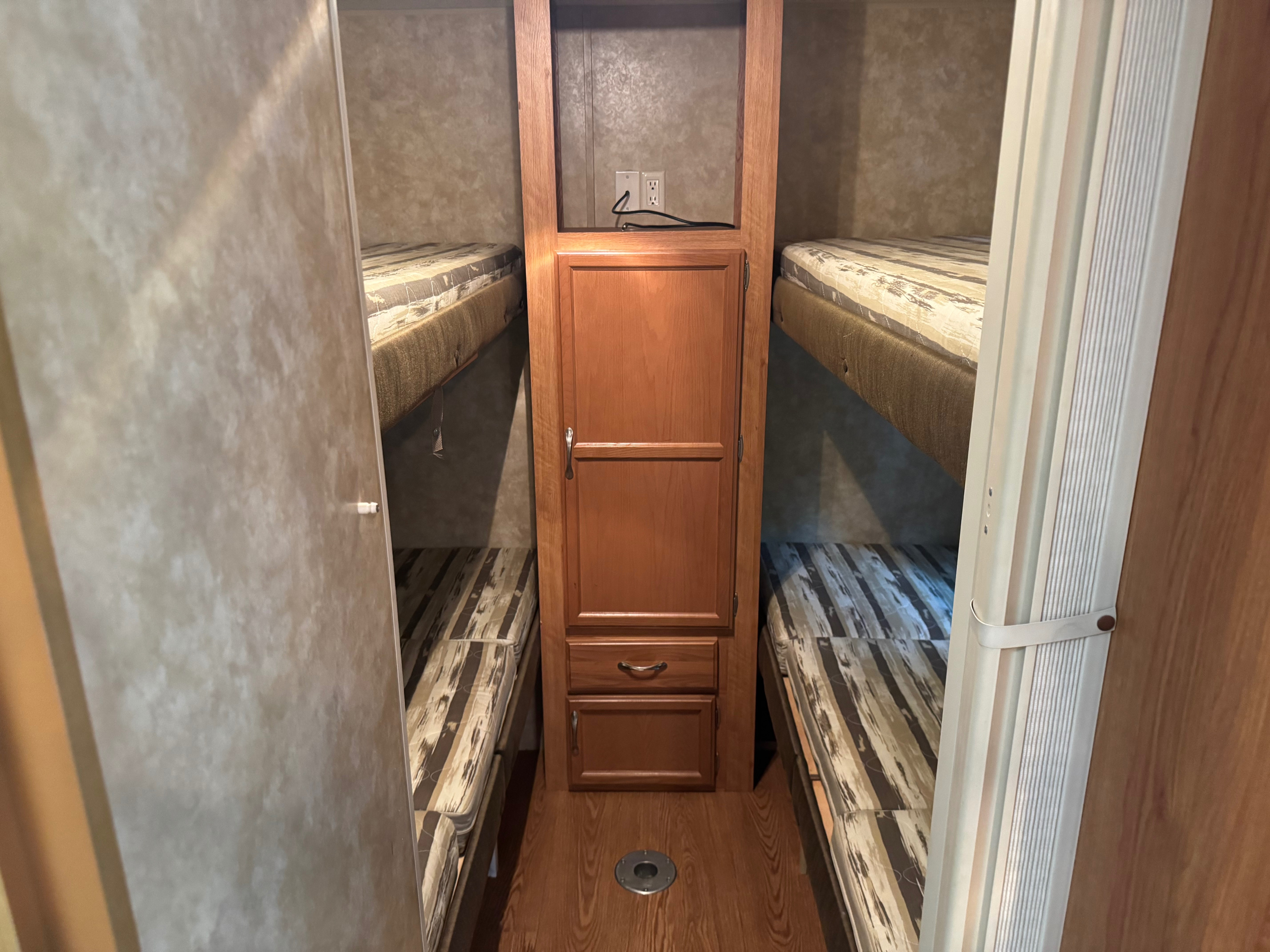 Inside an RV rental: Compact bunk beds flank a central wooden wardrobe with an outlet above.. Jayco Jay Flight G2 2008