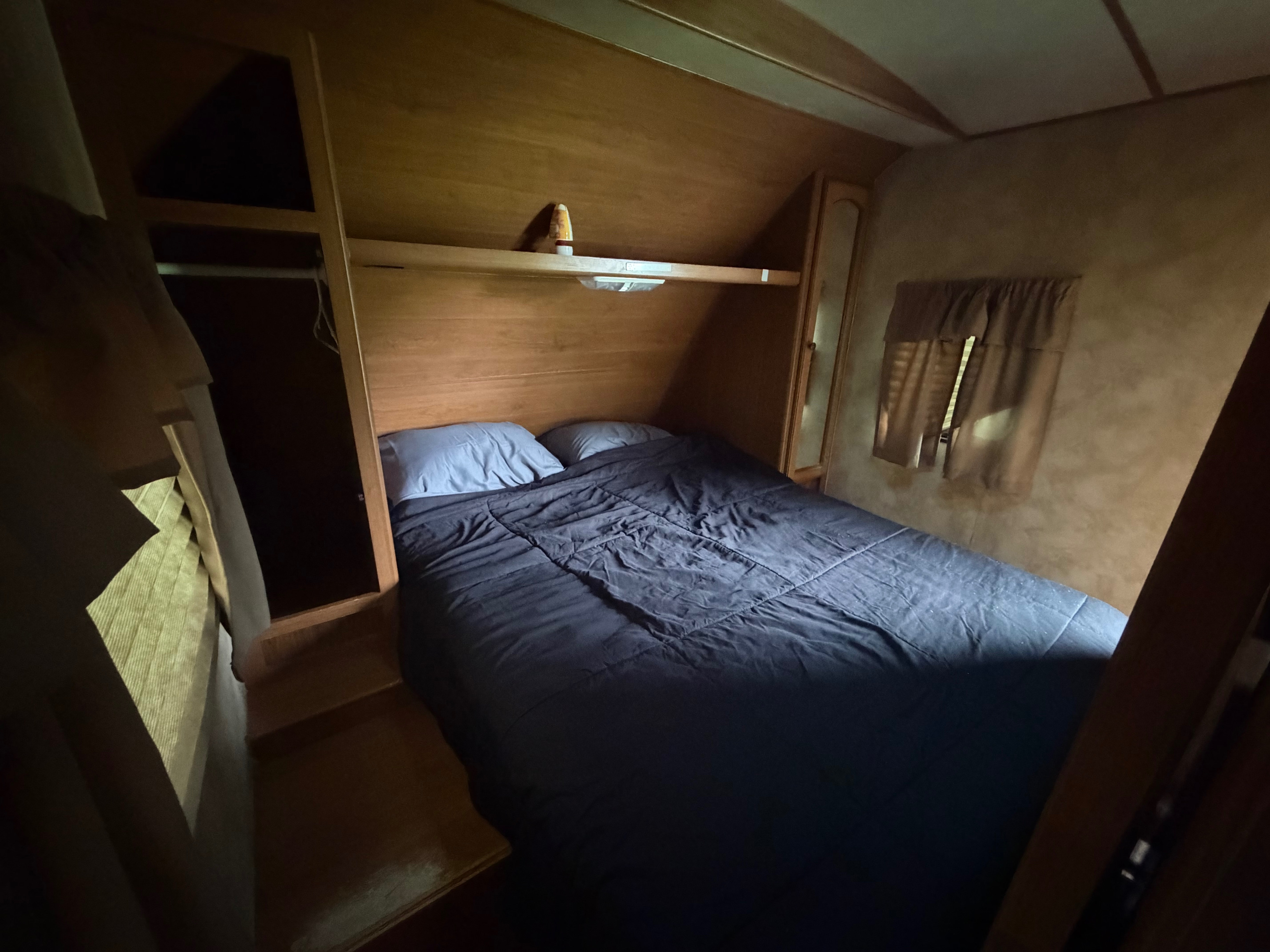 Compact rv rental bedroom with a comfy bed, dark bedding, and built-in wooden storage. Ready for your next adventure!. Crossroads RV Sunset Trail Super Lite 2015