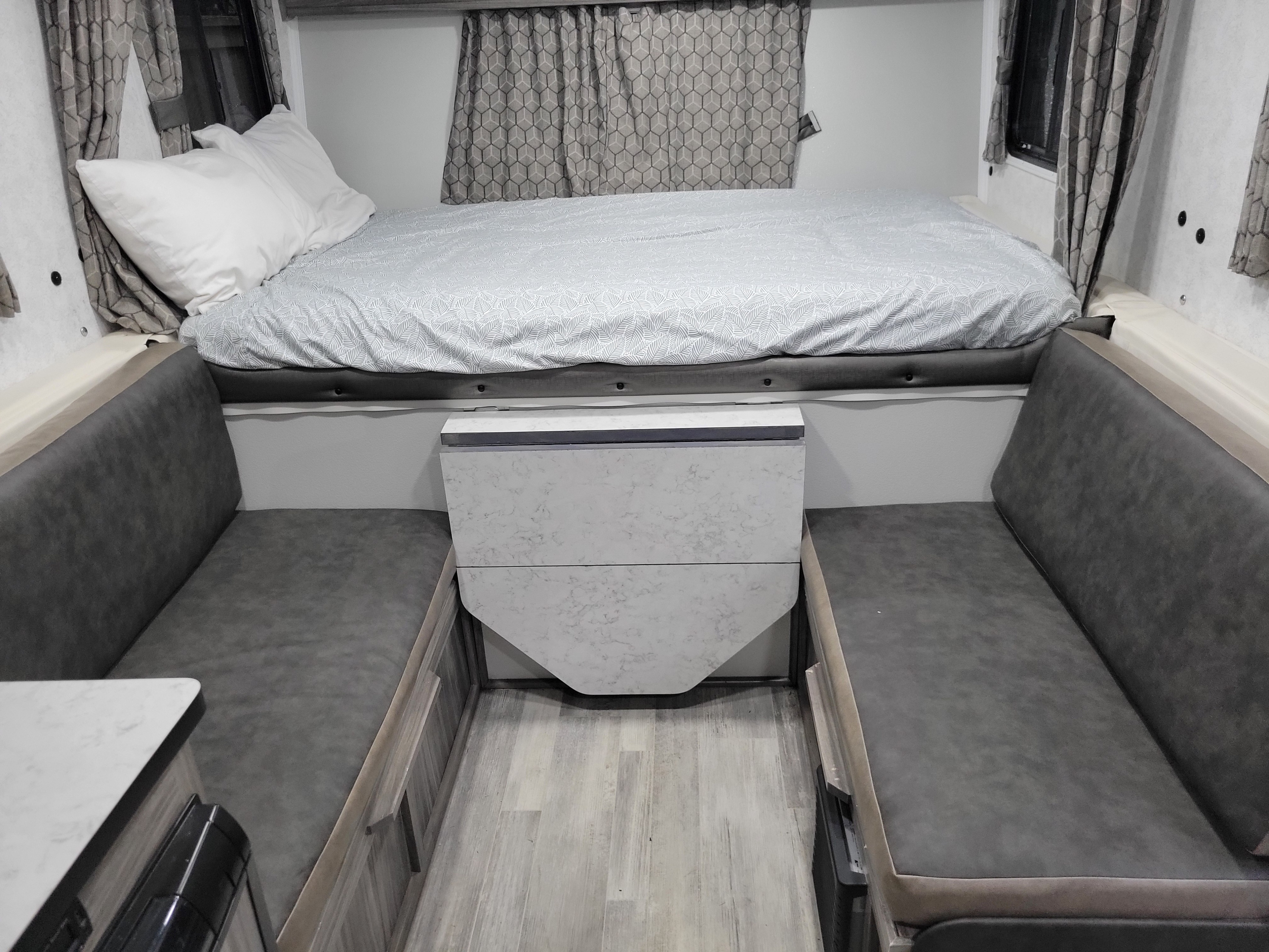 Explore this rv rental's compact interior, featuring a comfortable bed with patterned bedding, flanked by gray dinette seating.. TrailManor 2518KB 2022