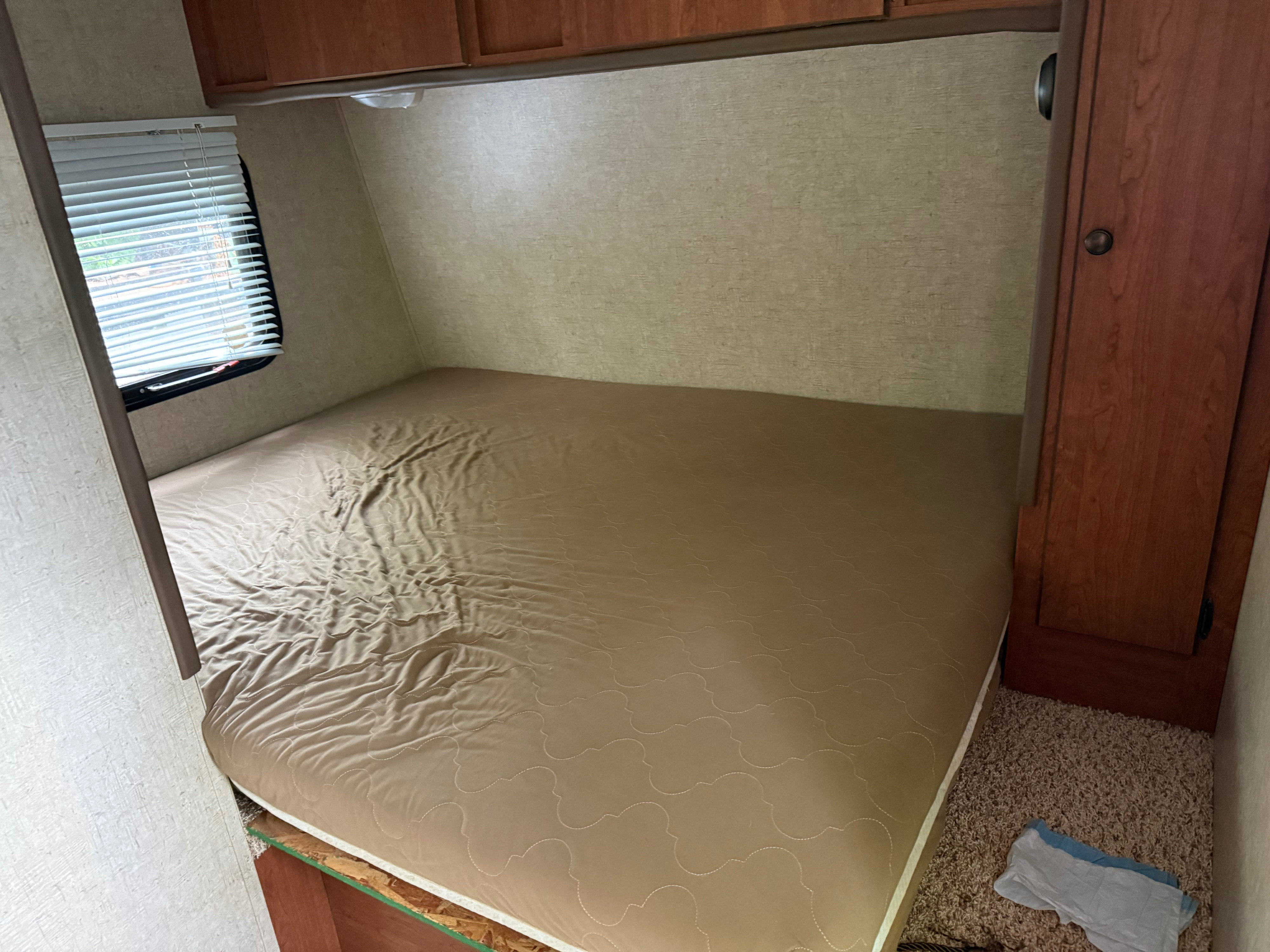 Compact RV rental bedroom with a bed, overhead wood cabinets, and a window with white blinds.. Sportsmen Classic 2013
