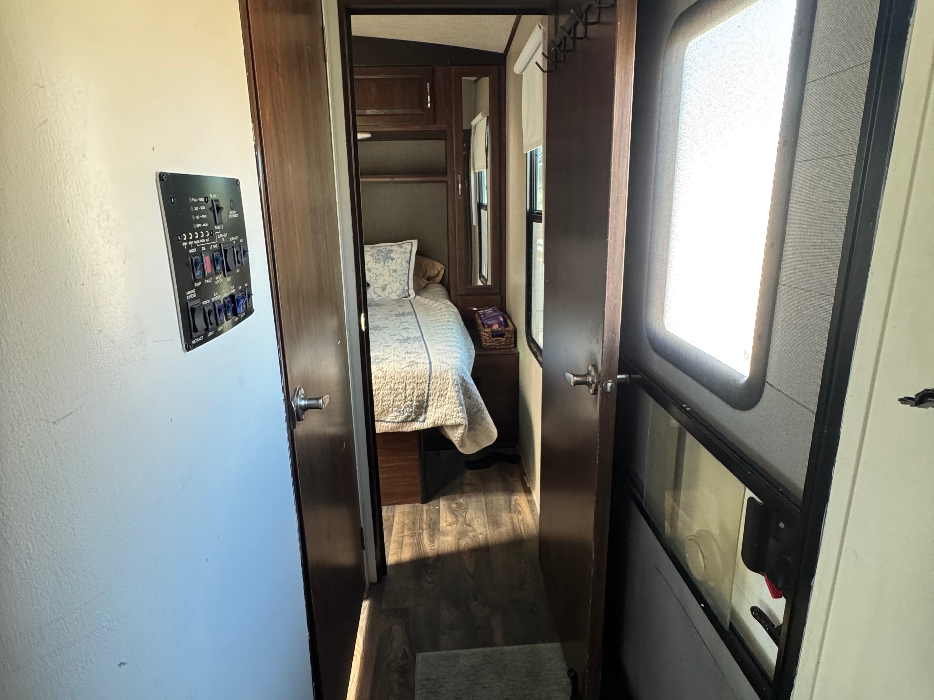 View inside an RV rental looking down a hallway towards the bedroom, with a control panel on the left and an entry door on the right.. Heartland Torque 2017