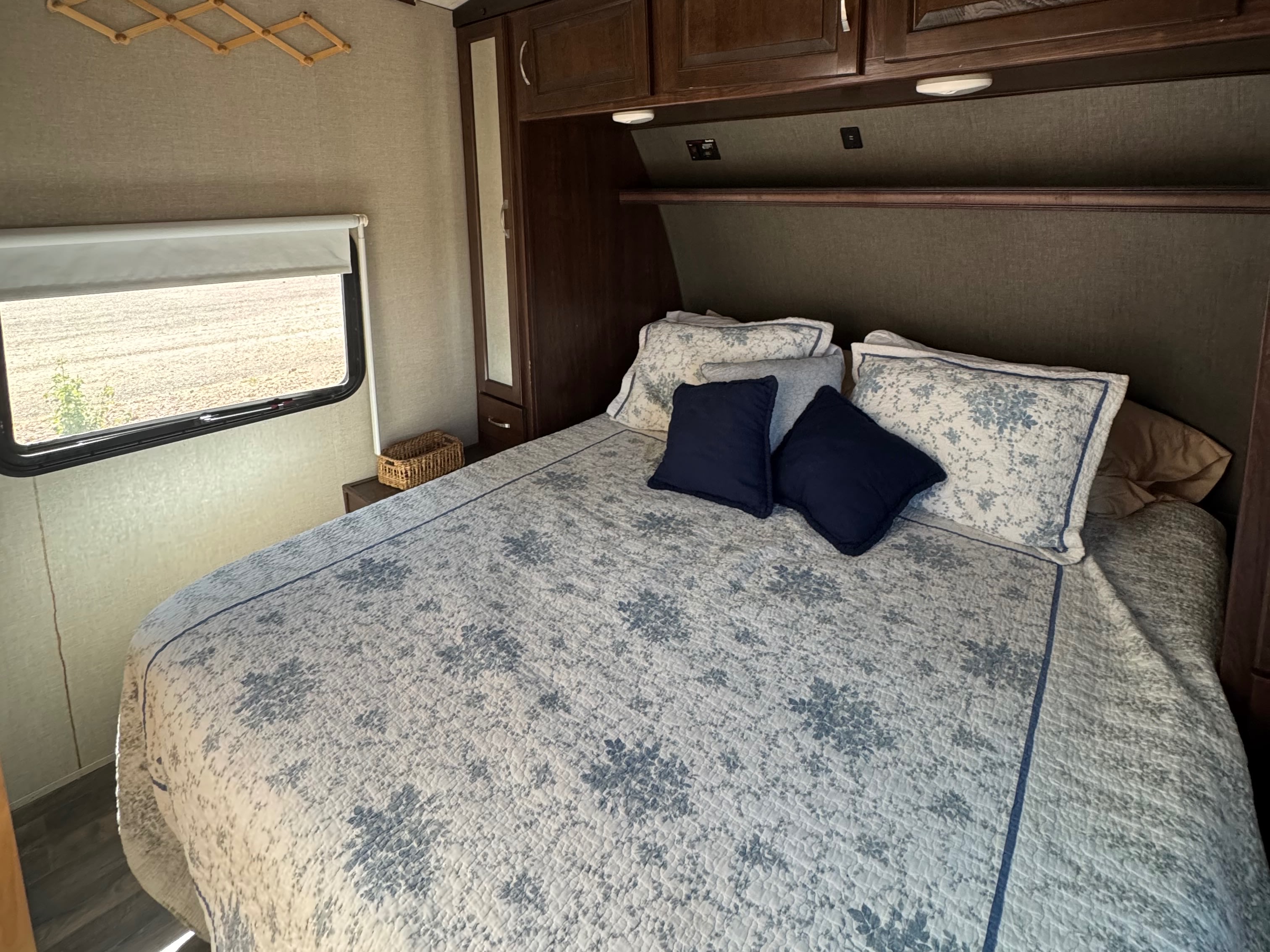 Cozy RV rental bedroom featuring a floral quilt, window view, and built-in storage for a comfortable stay.. Heartland Torque 2017