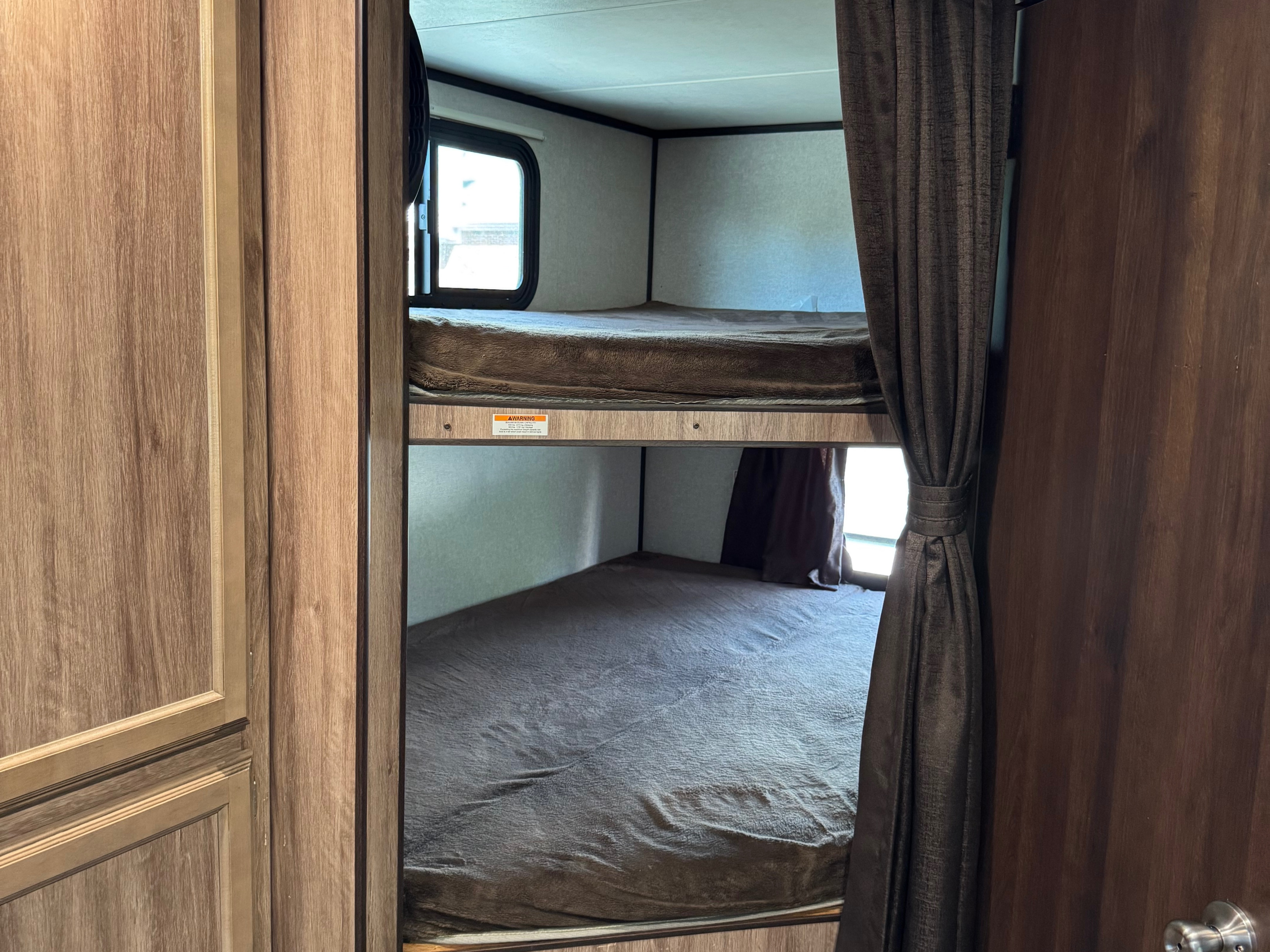Explore this RV rental's sleeping area, featuring cozy bunk beds with blankets, a window, and privacy curtains for comfort.. Jayco Jay Feather 2018