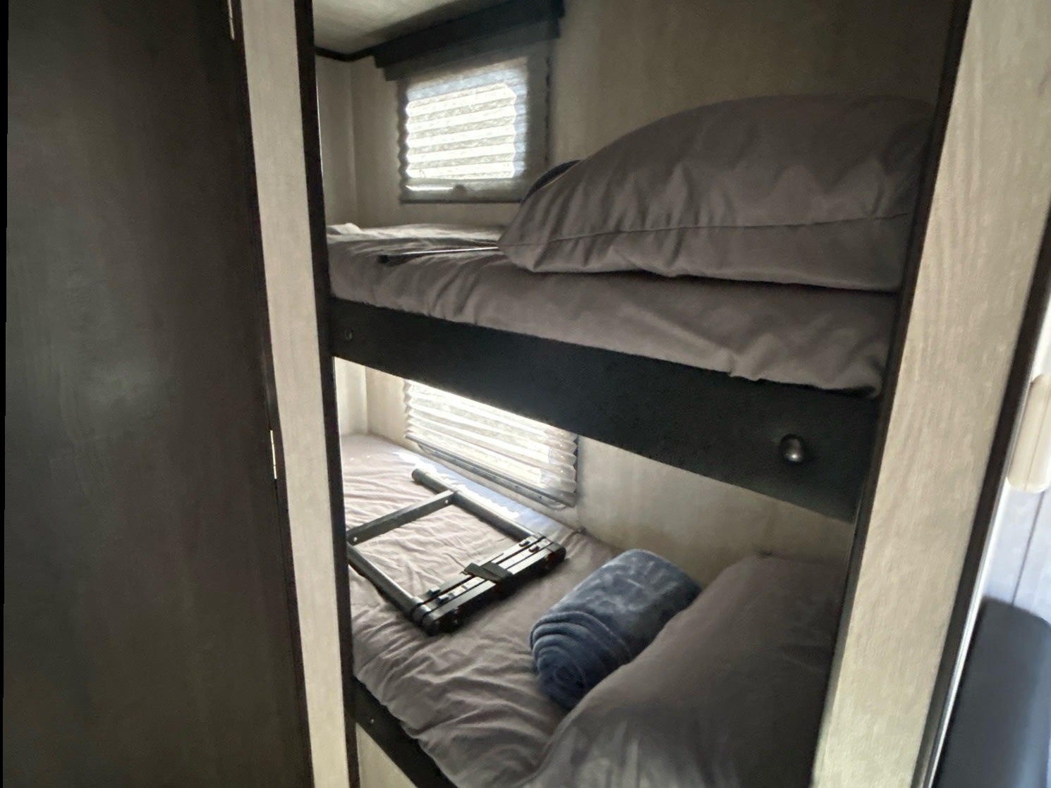 Compact RV rental bunk beds offer comfy sleeping. The lower bunk has a folded ladder and a rolled blue towel.. Genesis Supreme 16 BB 2024