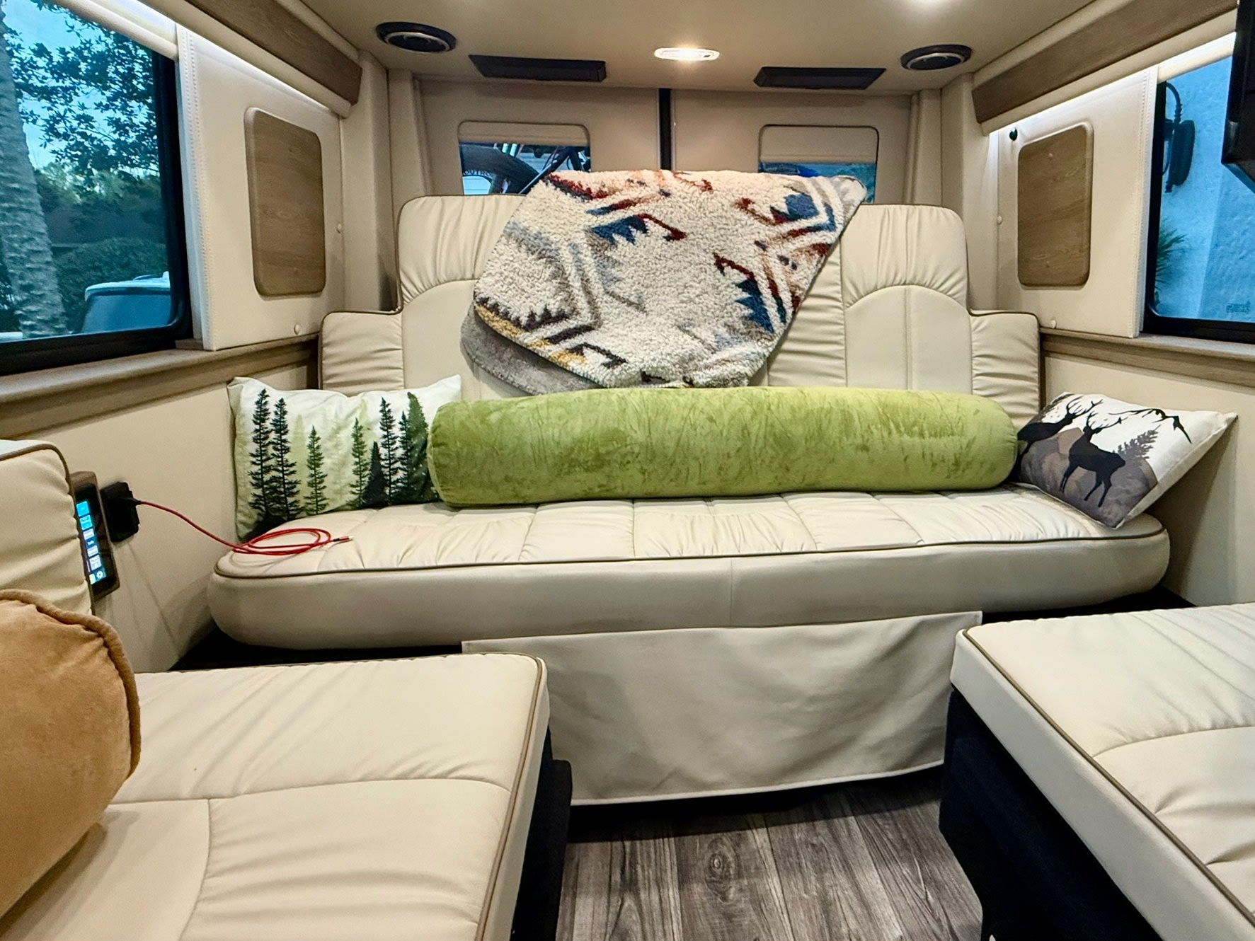 Relaxing RV rental interior: plush white seating, tree & deer pillows, and a cozy blanket for travel comfort.. Midwest Automotive Designs Midwest Automotive Designs Class B 2023