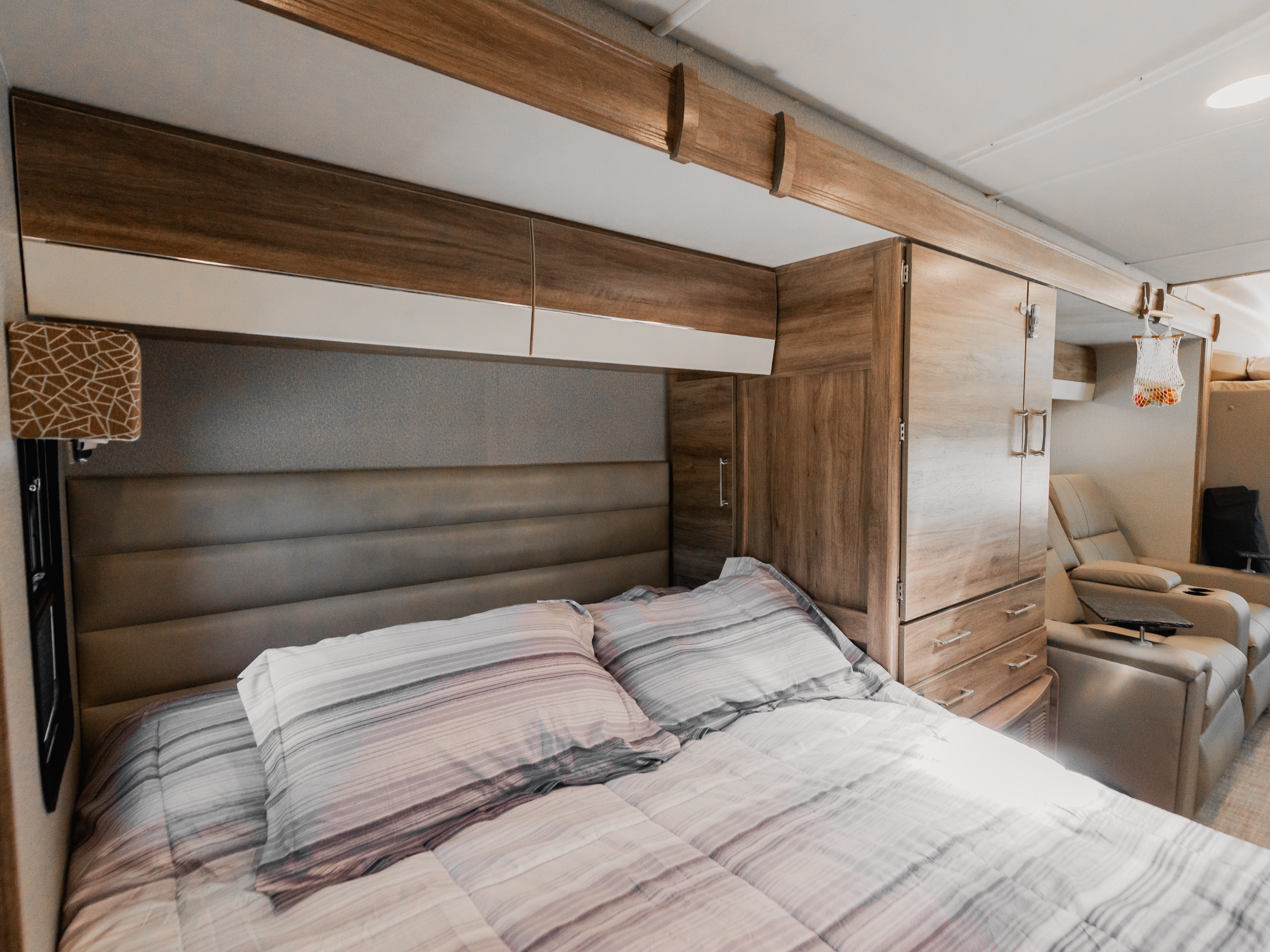 Comfortable RV rental bedroom featuring striped bedding, cushioned headboard, and wood overhead cabinets, perfect for travel.. Jayco Melbourne Prestige 2020