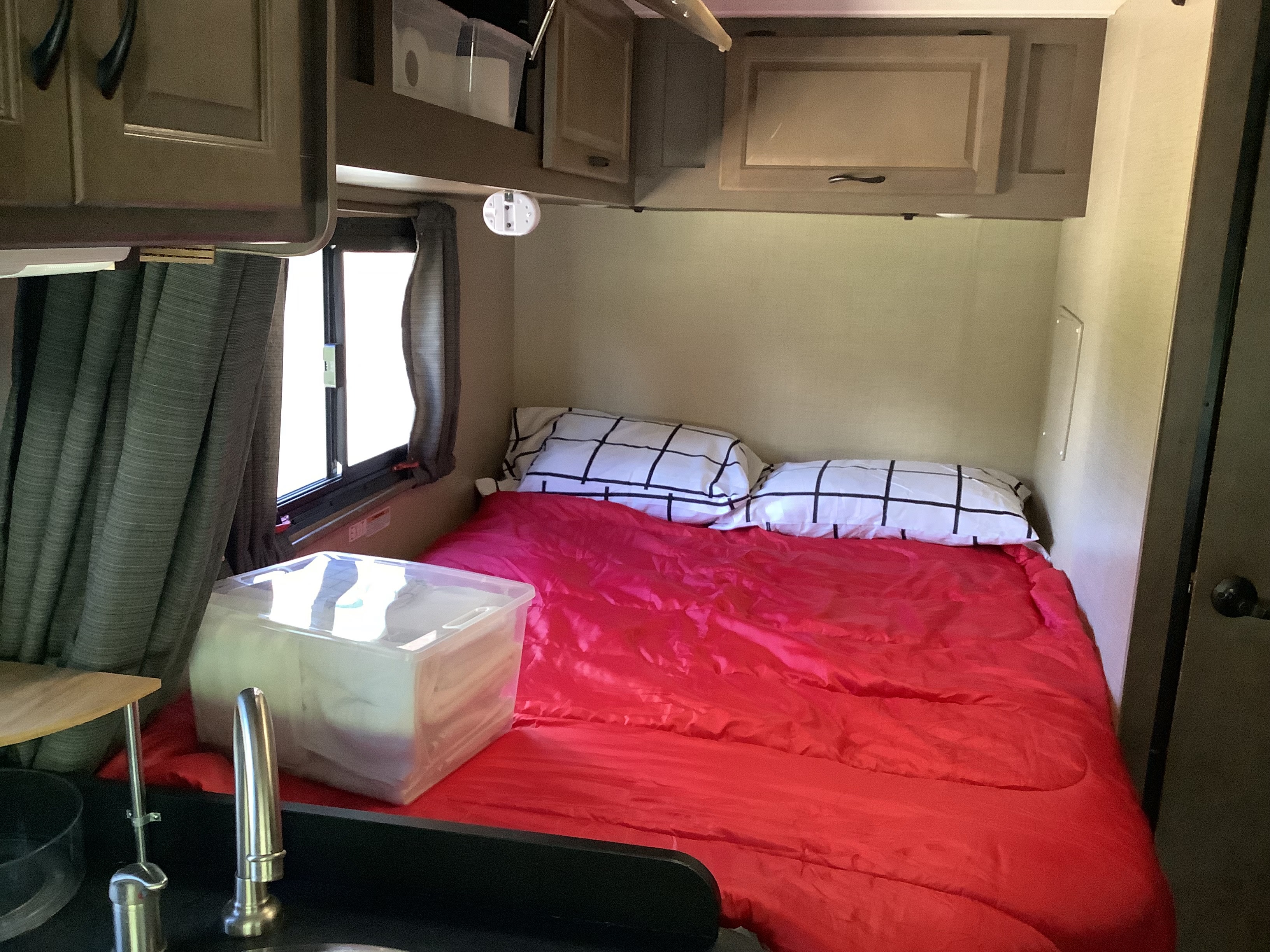 This RV rental bedroom features a comfy bed with a red comforter, patterned pillows, cabinets, and a small sink.. Thor Majestic 2018