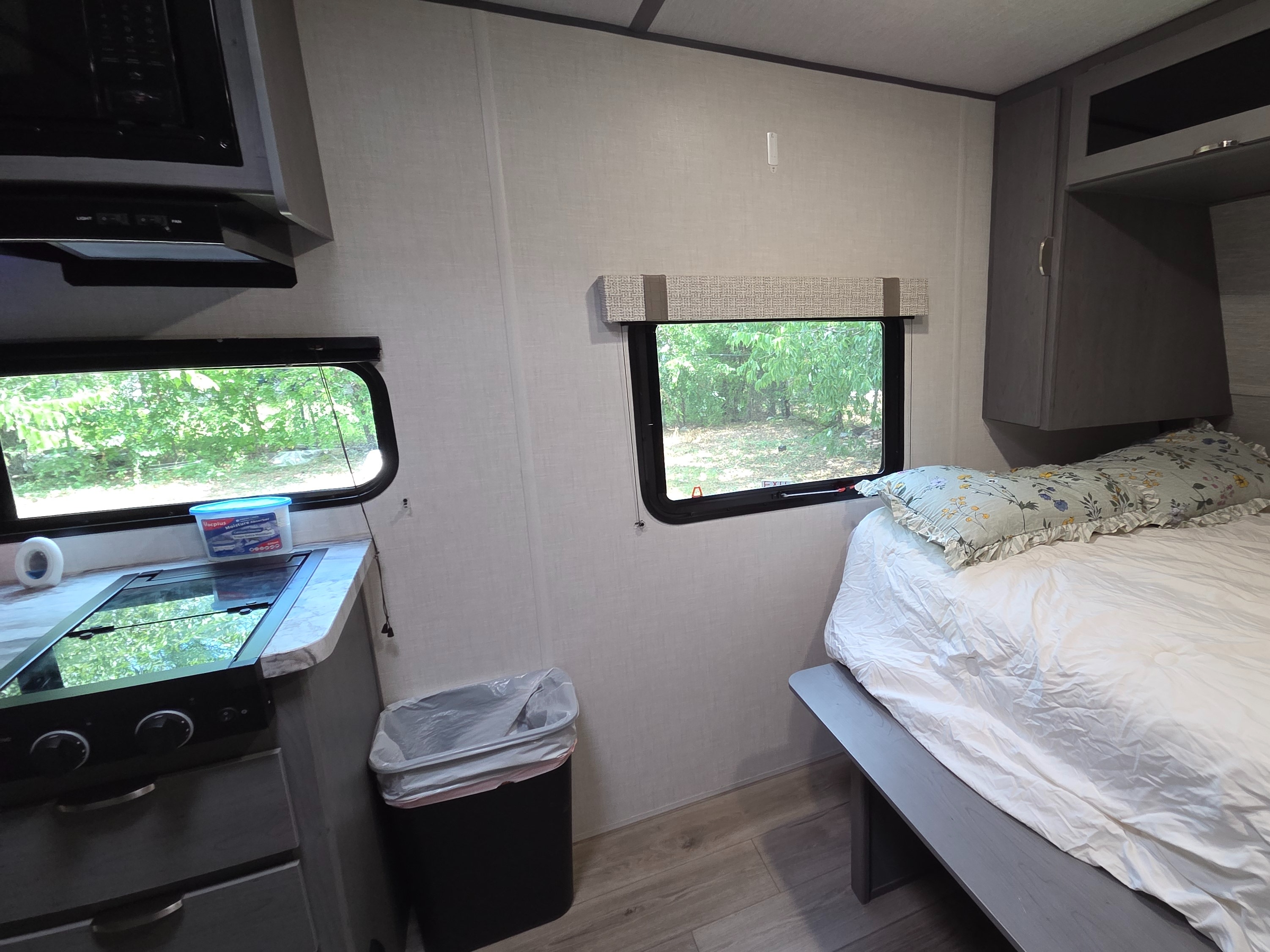 Compact RV rental interior featuring a kitchen with stovetop, a bed with floral pillows, and windows overlooking greenery.. Ozark Ozark Trailer 2025