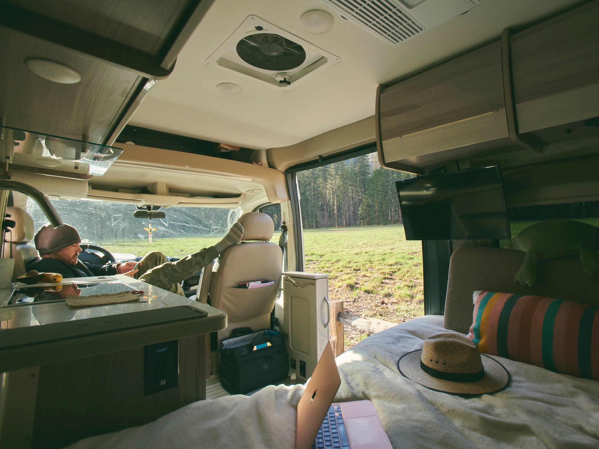 RV rental experience: Relax in a spacious camper van, with a person on a laptop and another on a phone, enjoying nature views.. Thor Sequence 2022