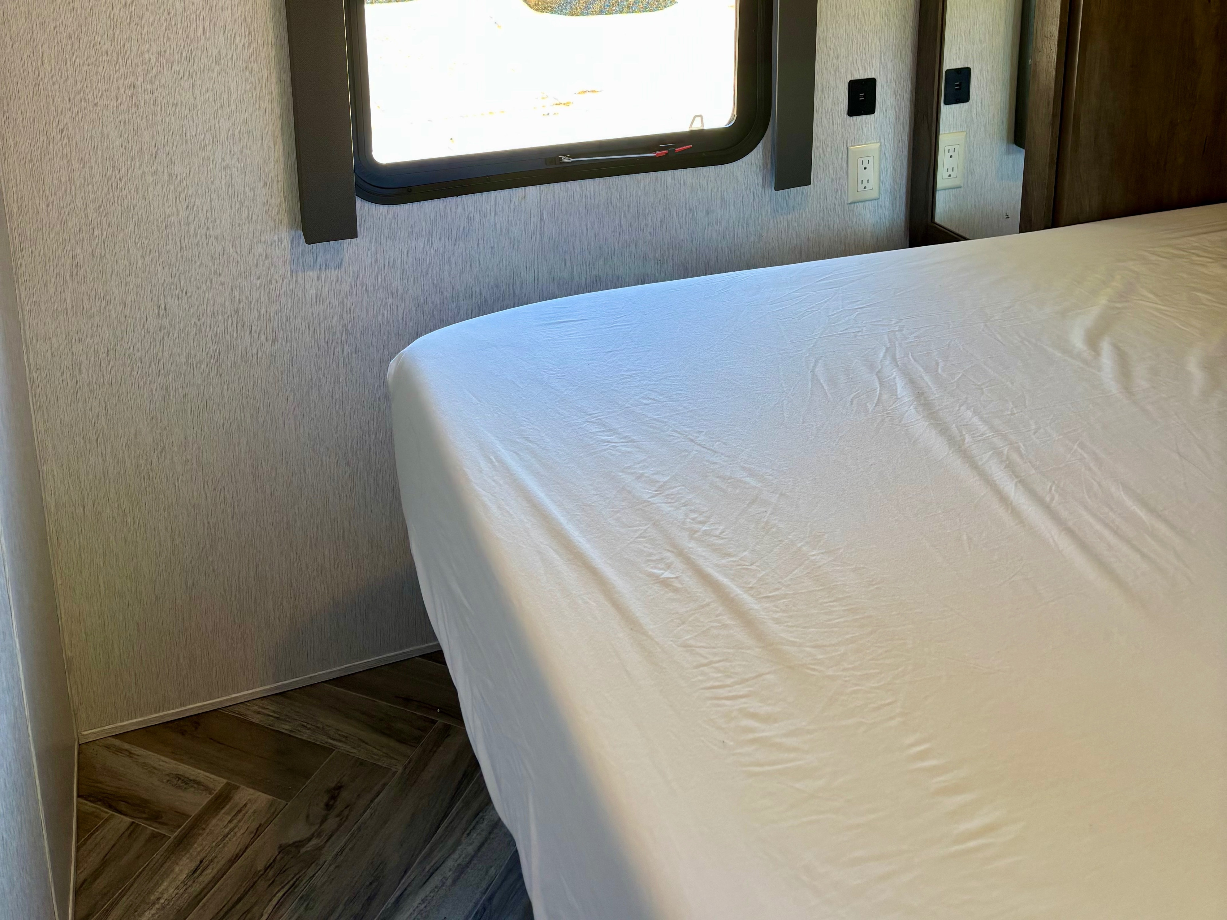 RV rental bedroom interior: white-sheeted bed, window, electrical outlets, and herringbone wood-look floor details visible.. Forest River Salem 2022