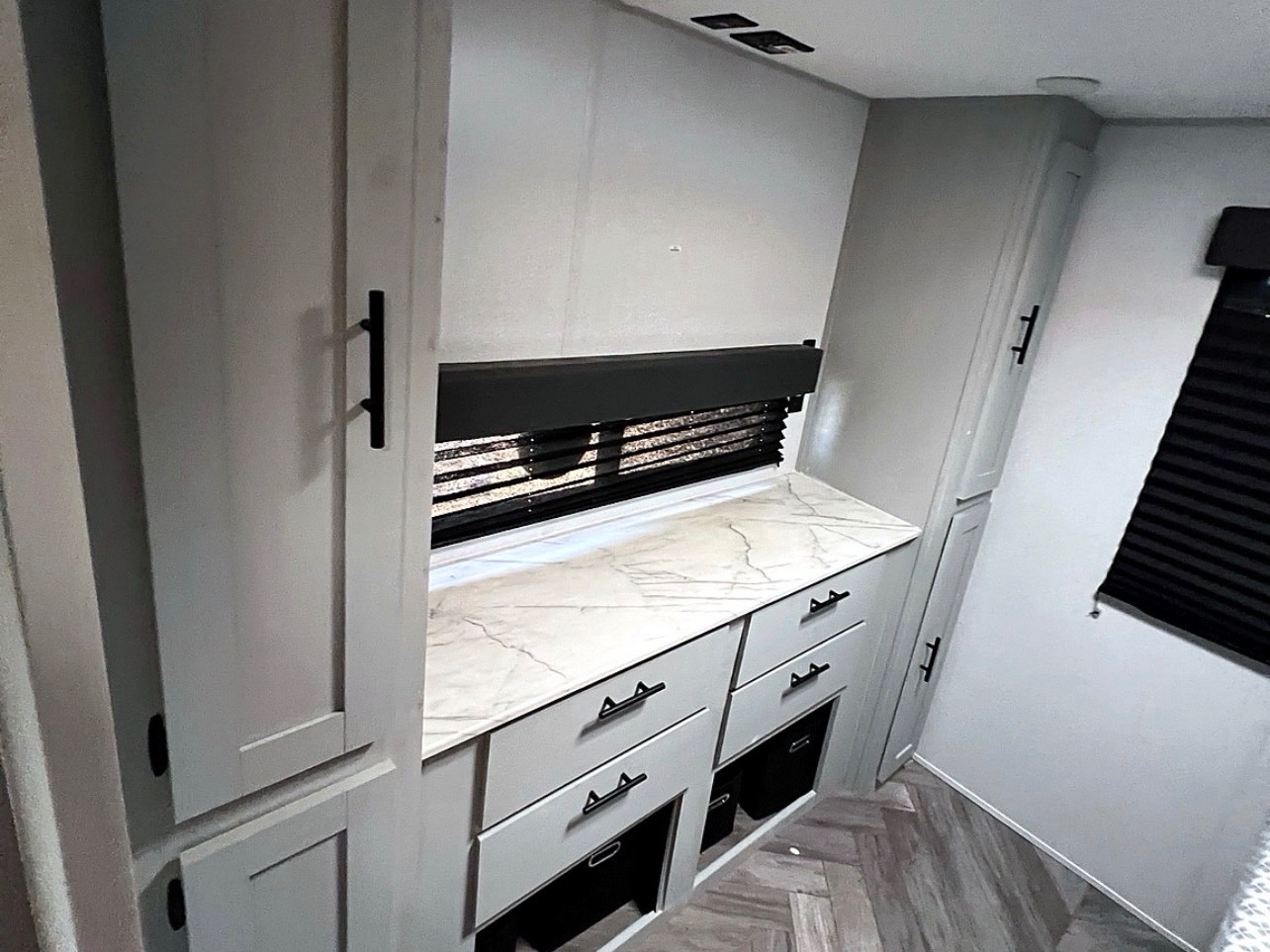 RV rental interior featuring light gray cabinets, a marble-look counter, dark window blinds, and tall storage units.. Forest River Wildwood FSX 2022