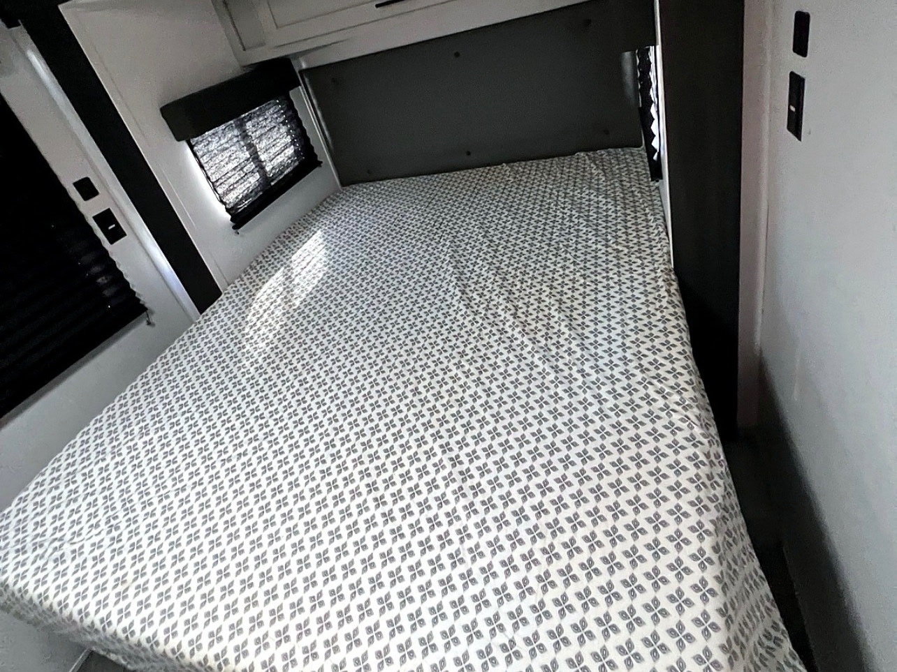 Comfortable RV rental bedroom with a gray patterned bed, window with blinds, and white/dark interior. Ideal for your journey.. Forest River Wildwood FSX 2022