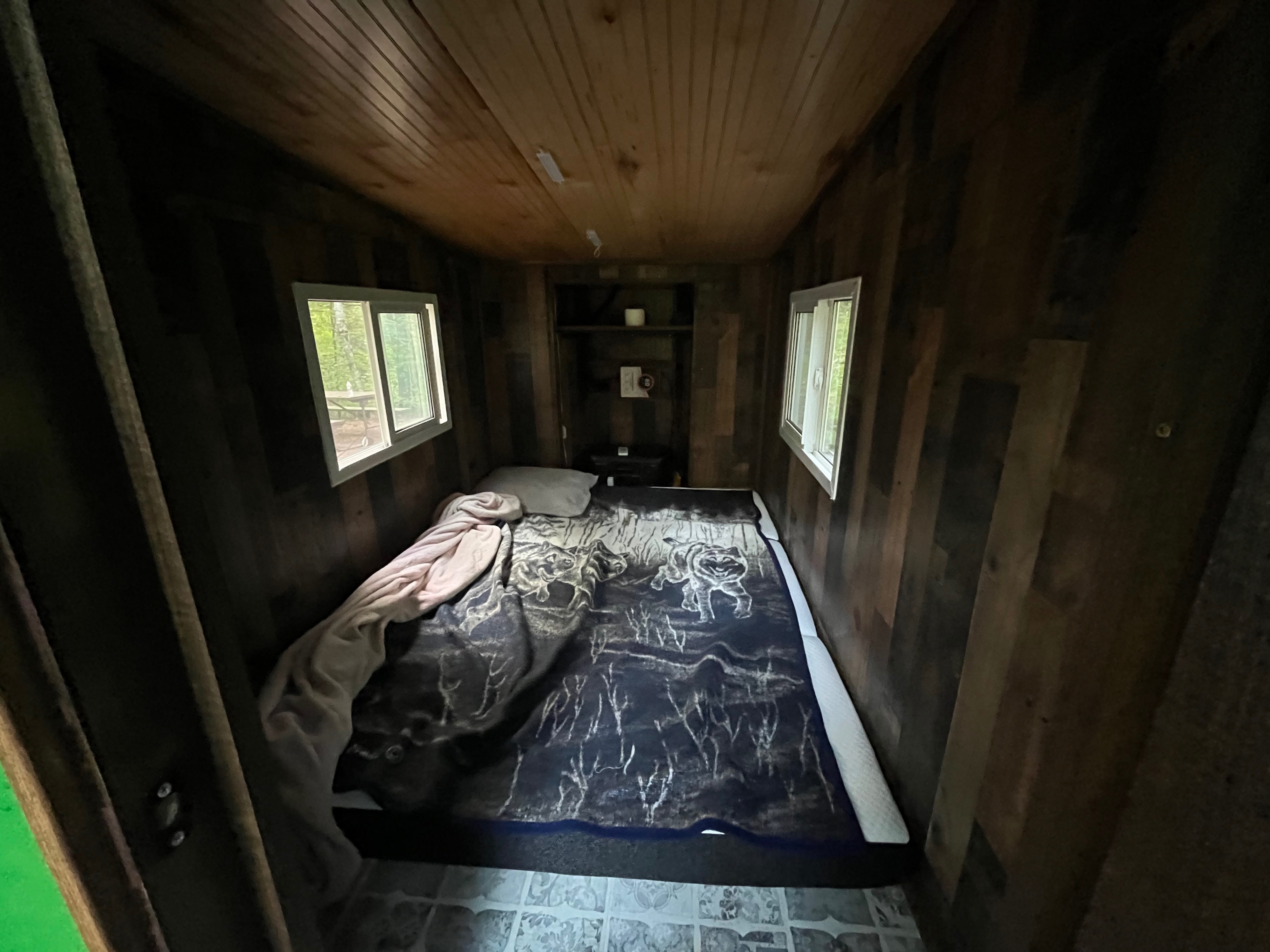 Cozy RV rental bedroom with rustic wood paneling, a bed featuring a wolf-patterned blanket, and serene nature views from windows.. Custom Custom 2025