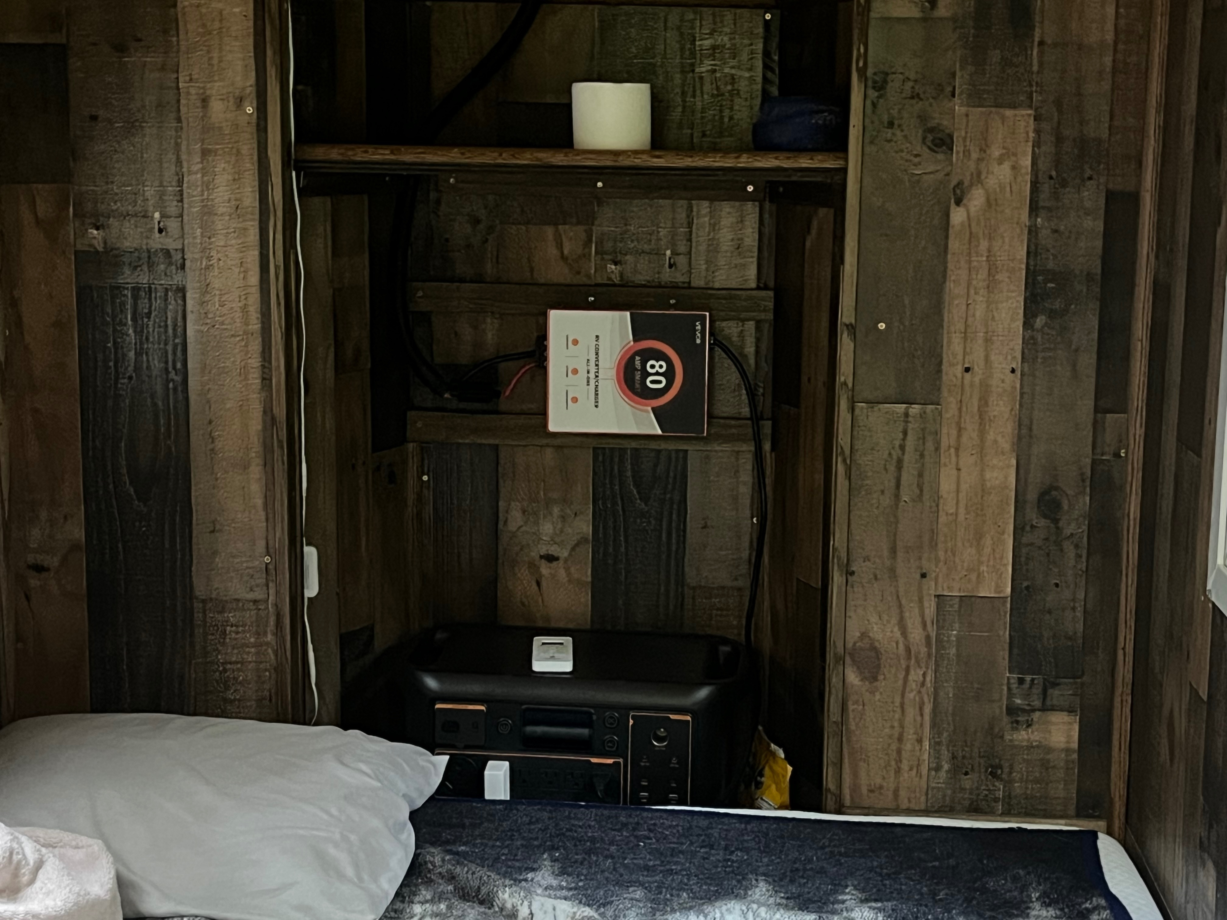 RV rental interior featuring a practical power setup: 80 AMP smart converter charger & portable power station. Bed & rustic wood walls.. Custom Custom 2025