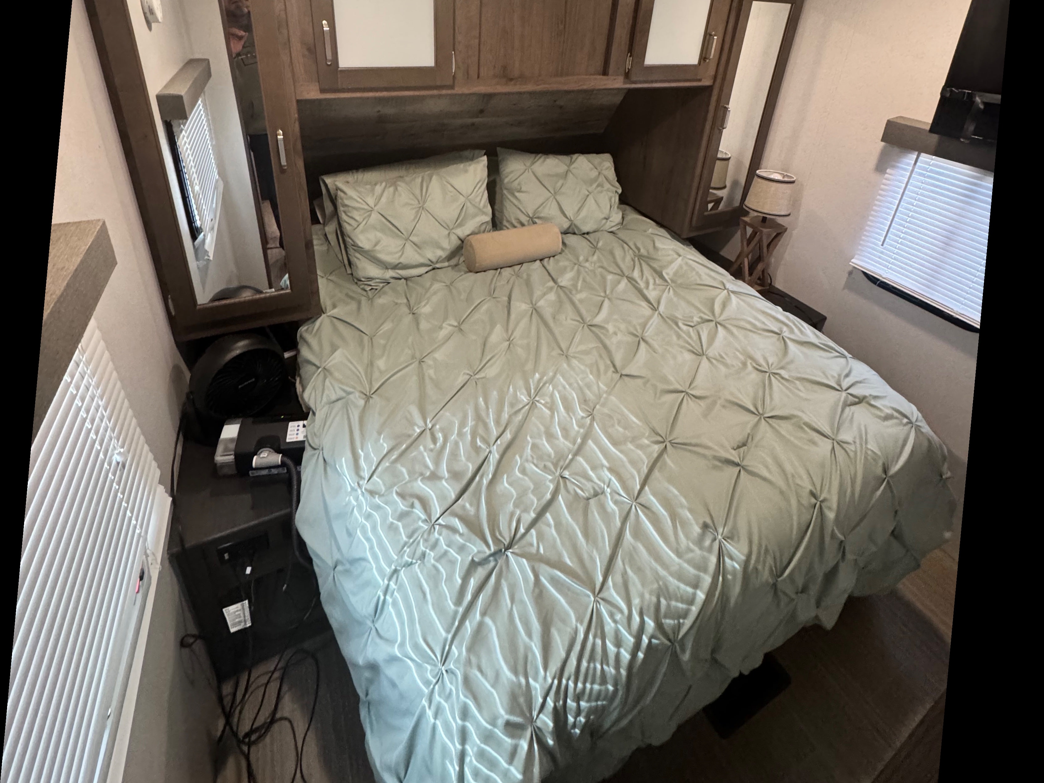 Cozy RV rental bedroom featuring a bed with light green bedding, overhead cabinets, a fan, and a bedside lamp.. Keystone RV Passport Grand Touring 2020