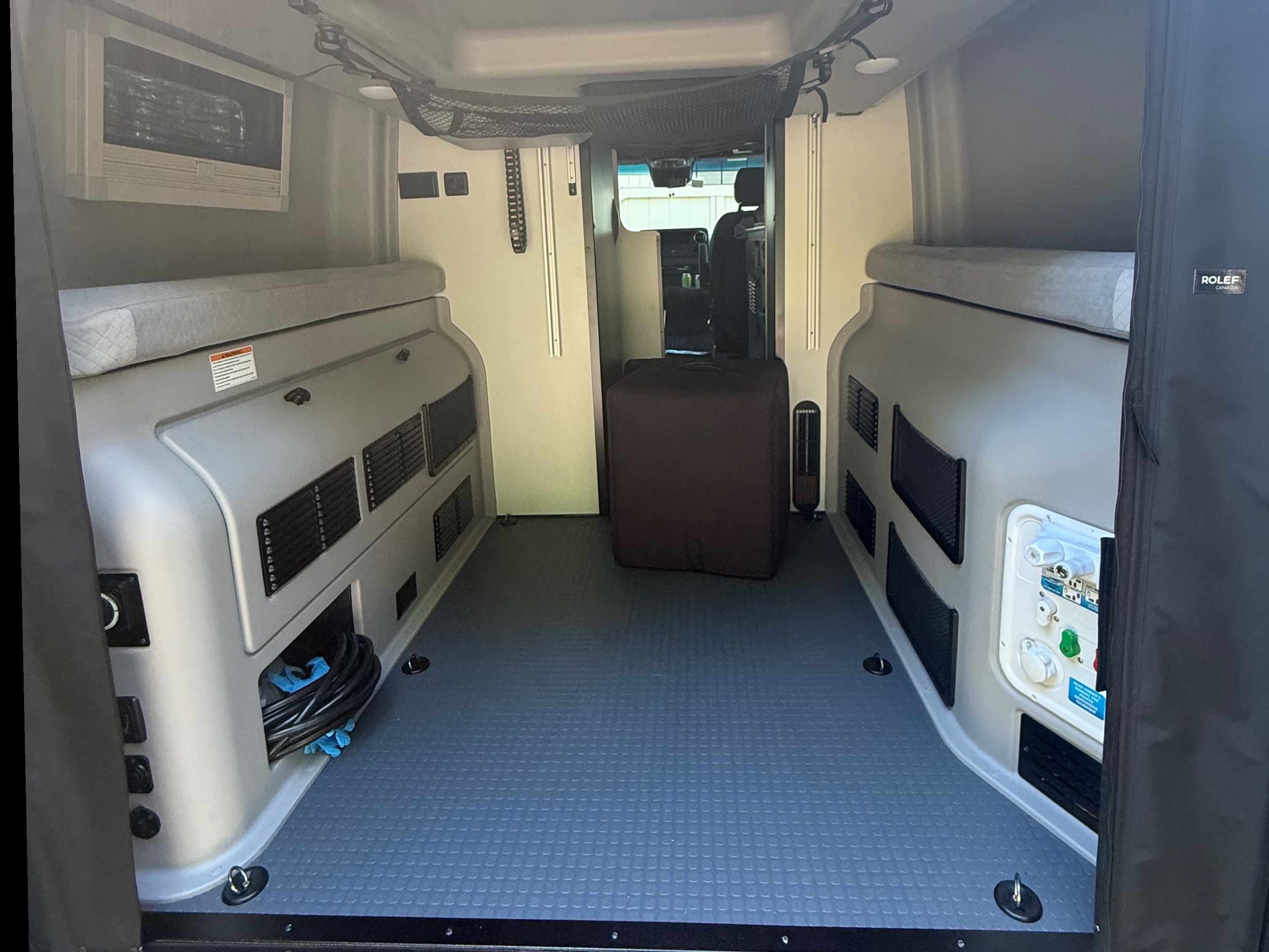 Inside an rv rental: rear view of utility-lined walls, comfortable bench beds, and textured floor with tie-downs.. Winnebago Revel 2025