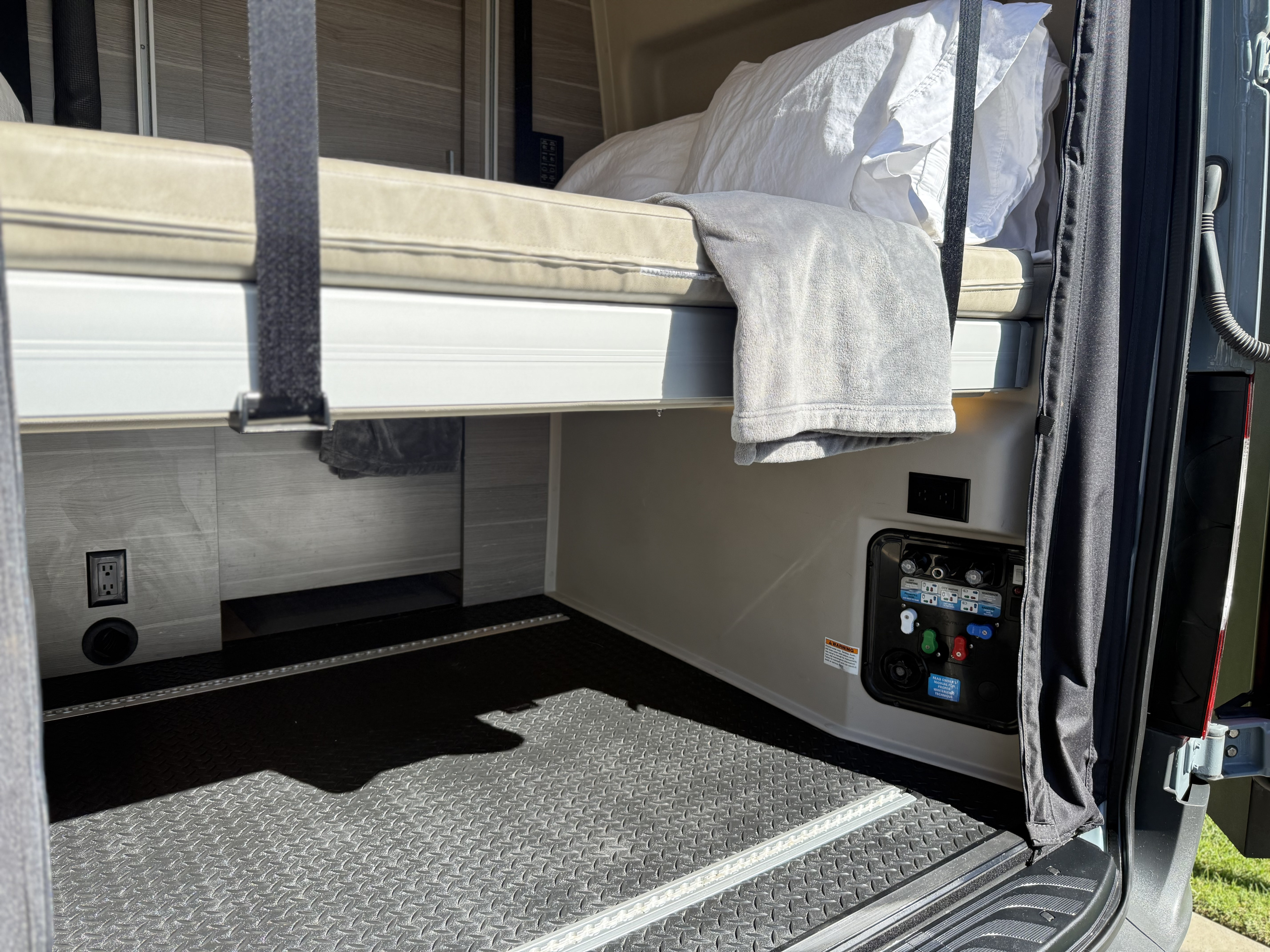RV rental campervan interior: bunk bed, water utility panel, electrical outlet, and functional cargo area.. Jayco Terrain 2023