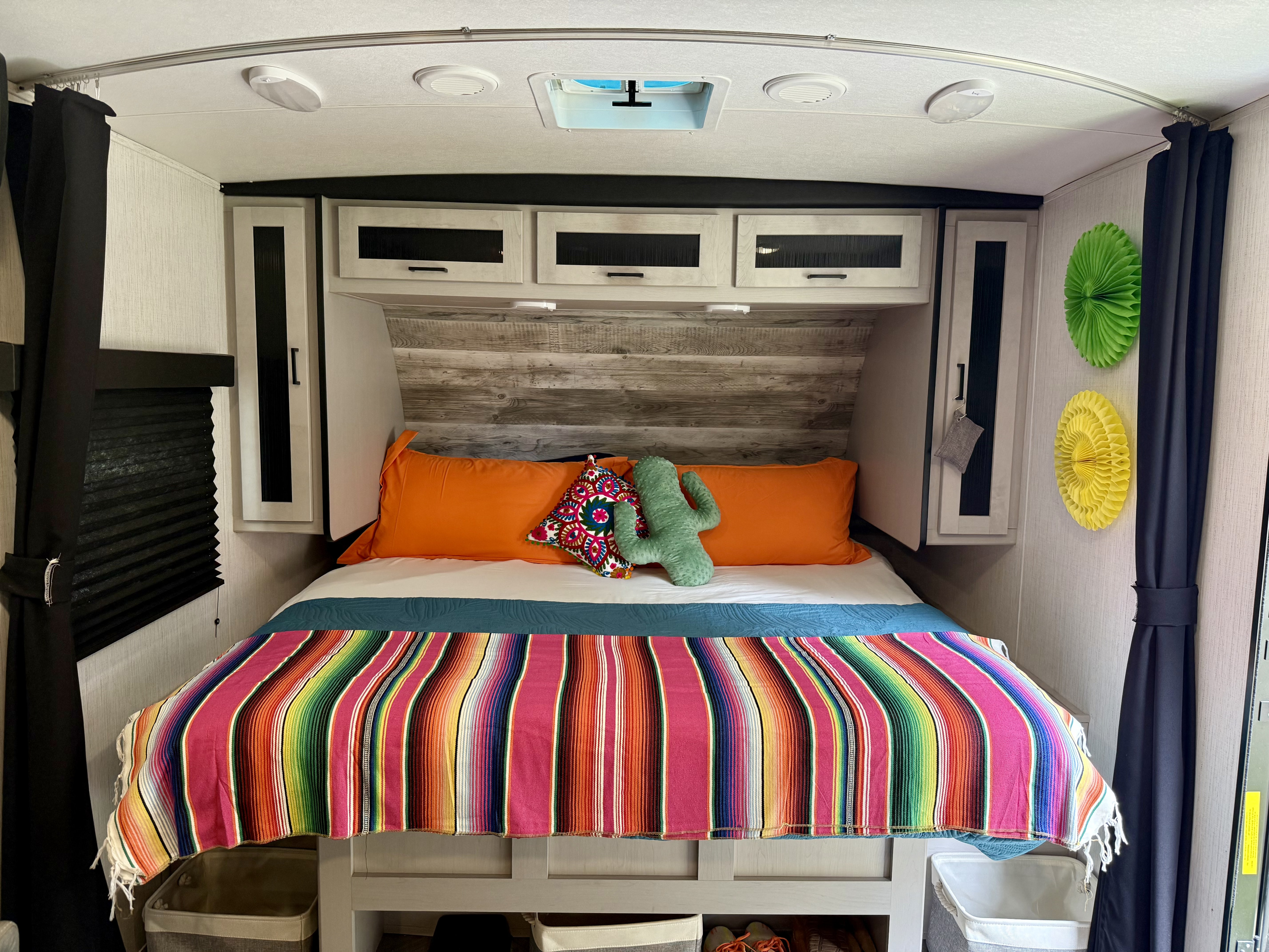Cozy RV rental bedroom with a colorful striped blanket, orange pillows, overhead cabinets, and blackout curtains.. Heartland Mallard 2023
