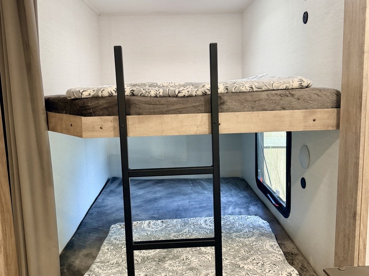Enjoy an RV rental's cozy bunk beds! Features a ladder, soft blankets, and a window in the lower sleeping area.. Gulf Stream Enlighten SE 2025