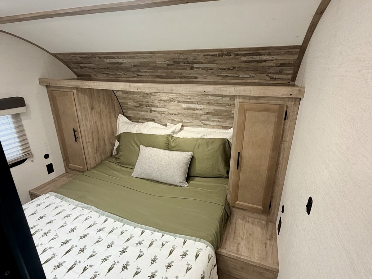Cozy RV rental bedroom features an olive green bed with built-in storage and rustic wood accents. Ideal for travel!. Gulf Stream Enlighten SE 2025