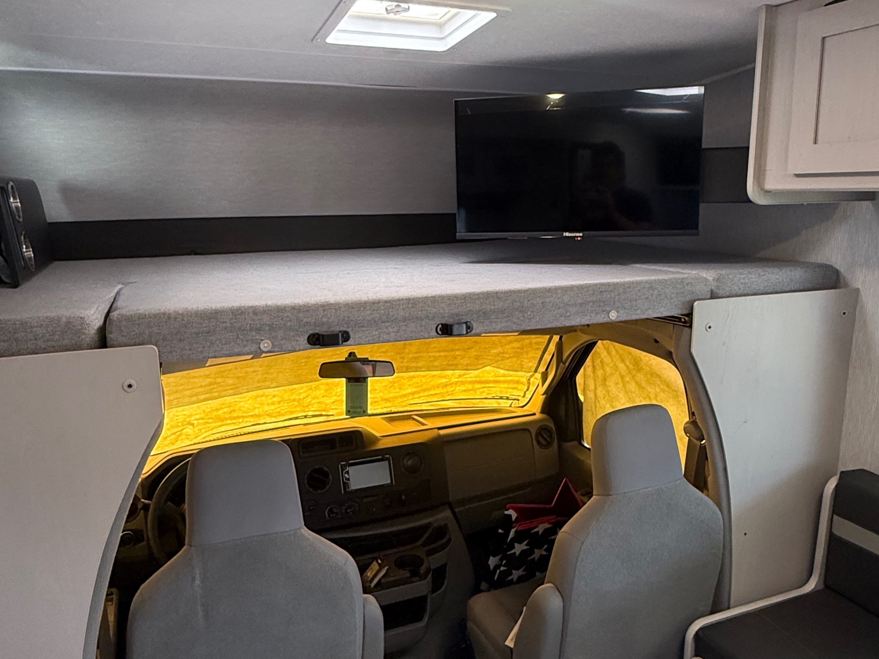 RV rental interior showing overhead bed, cab area with a yellow sunshade, and a mounted TV.. Forest River Coachmen Freelander 2023