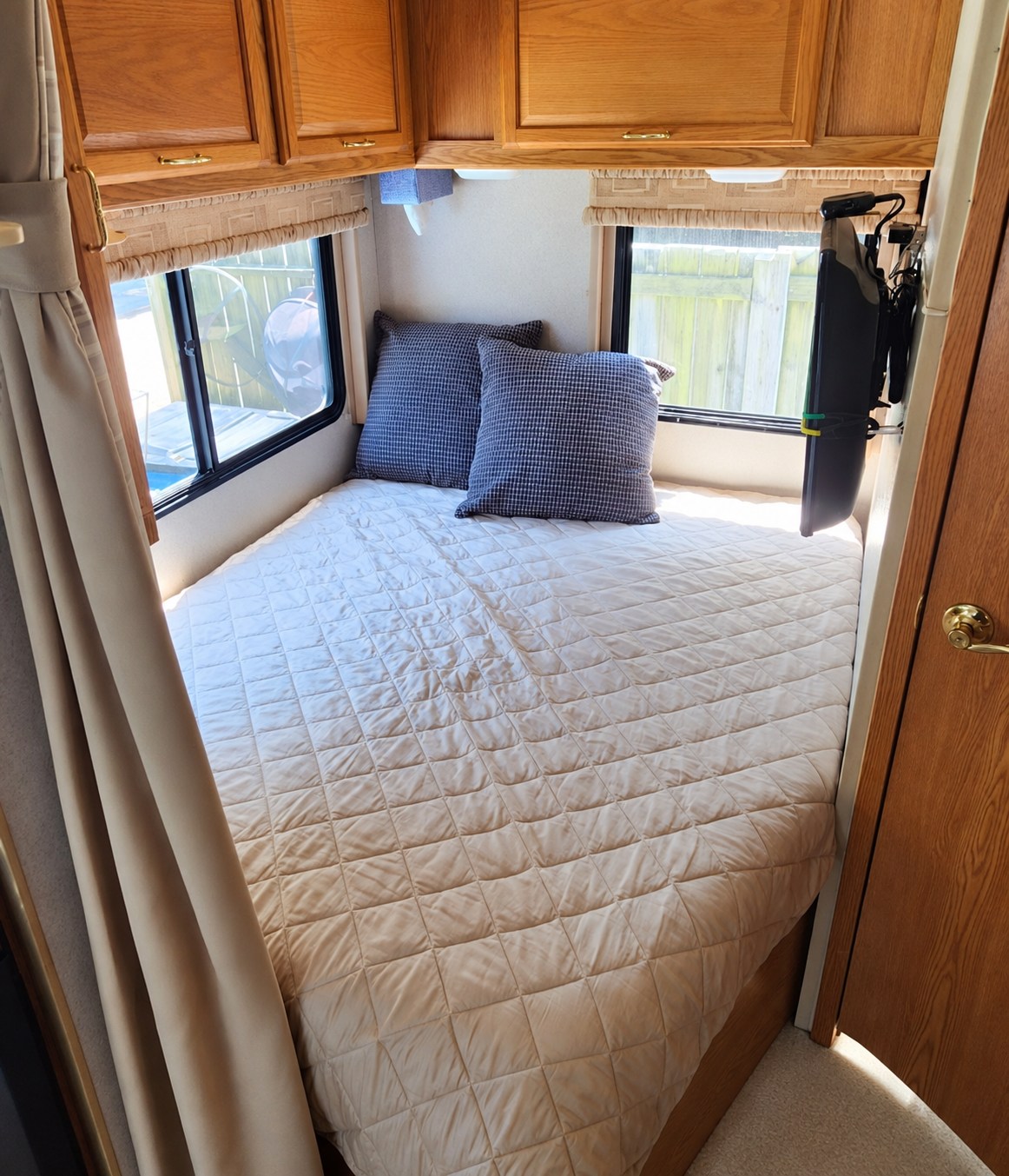 Explore this cozy RV rental bedroom: quilted bed, pillows, wooden cabinets, and windows for comfortable travel accommodation.. Winnebago Minnie Winnie 2004