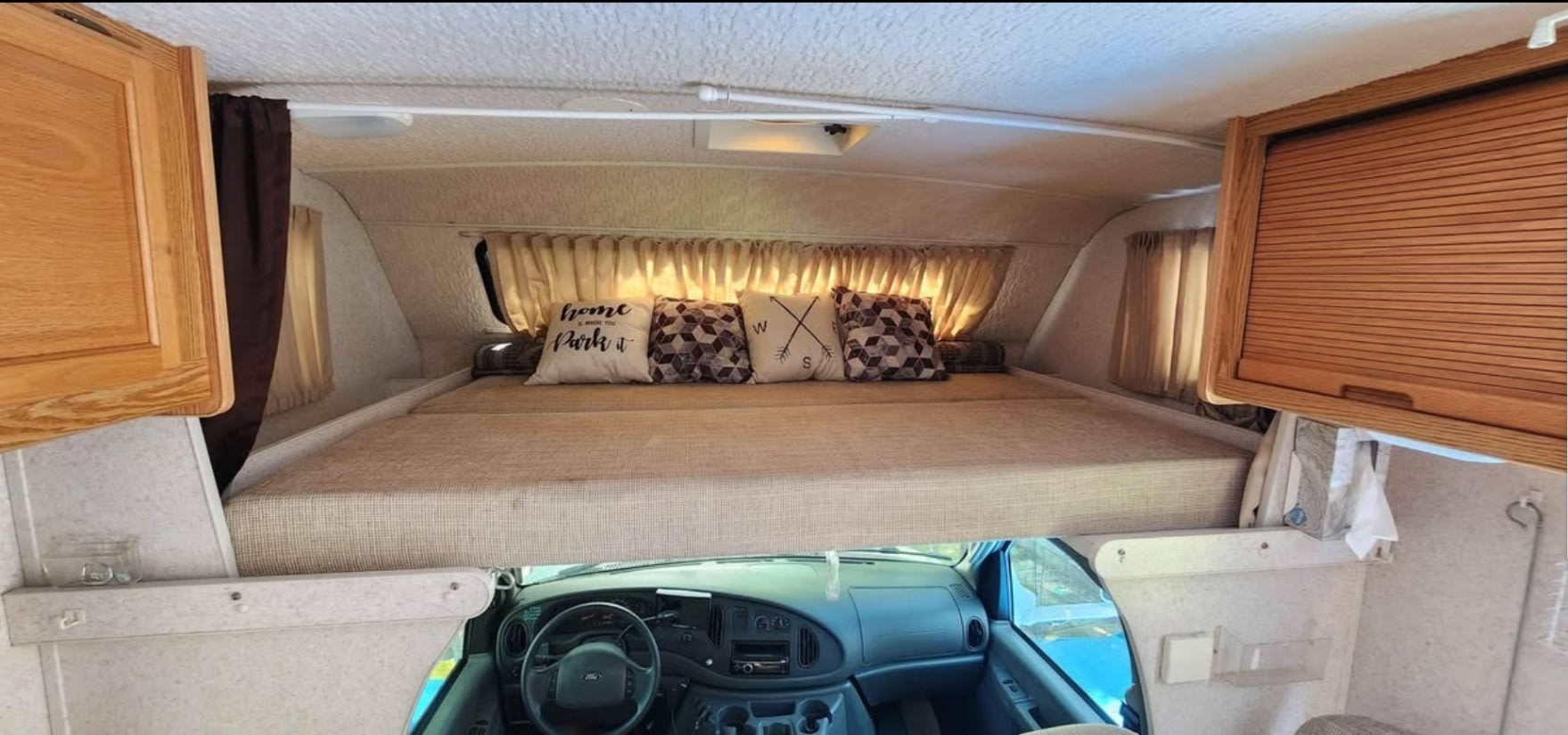 Inside an RV rental: a comfortable cab-over bunk with decorative pillows above the driver's cockpit area.. Winnebago Minnie Winnie 2004