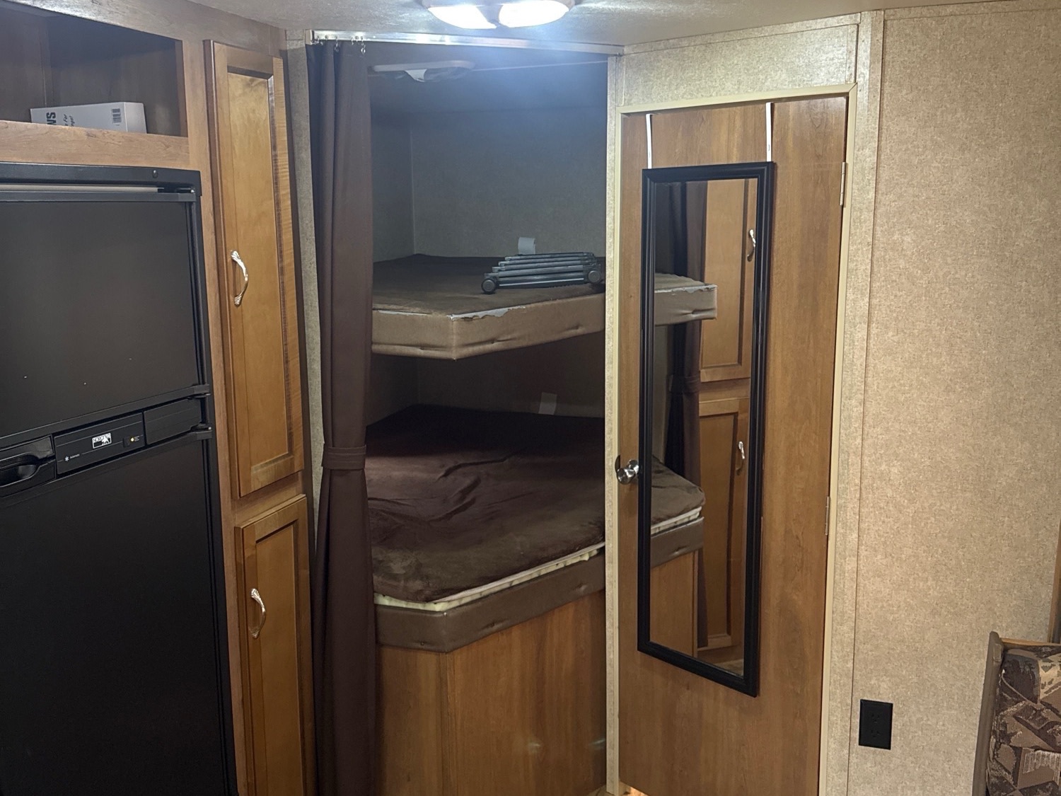 Inside an rv rental: Cozy bunk beds with a privacy curtain, next to a black fridge and wood storage for compact living.. Coachmen Catalina 2016