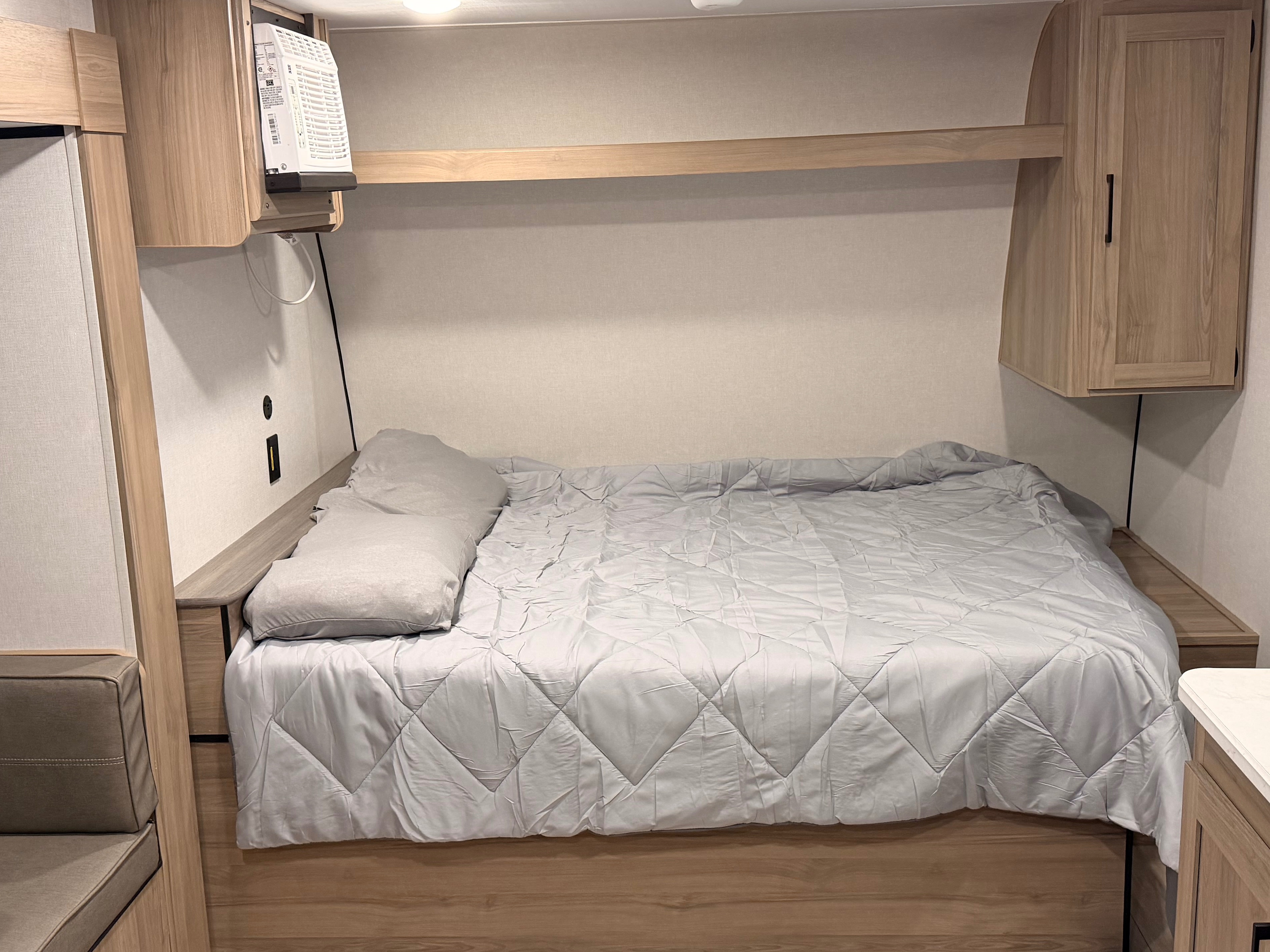 Cozy RV rental bedroom featuring a comfortable bed, light wood accents, overhead storage, and a convenient charging station.. Keystone RV Coleman 2026