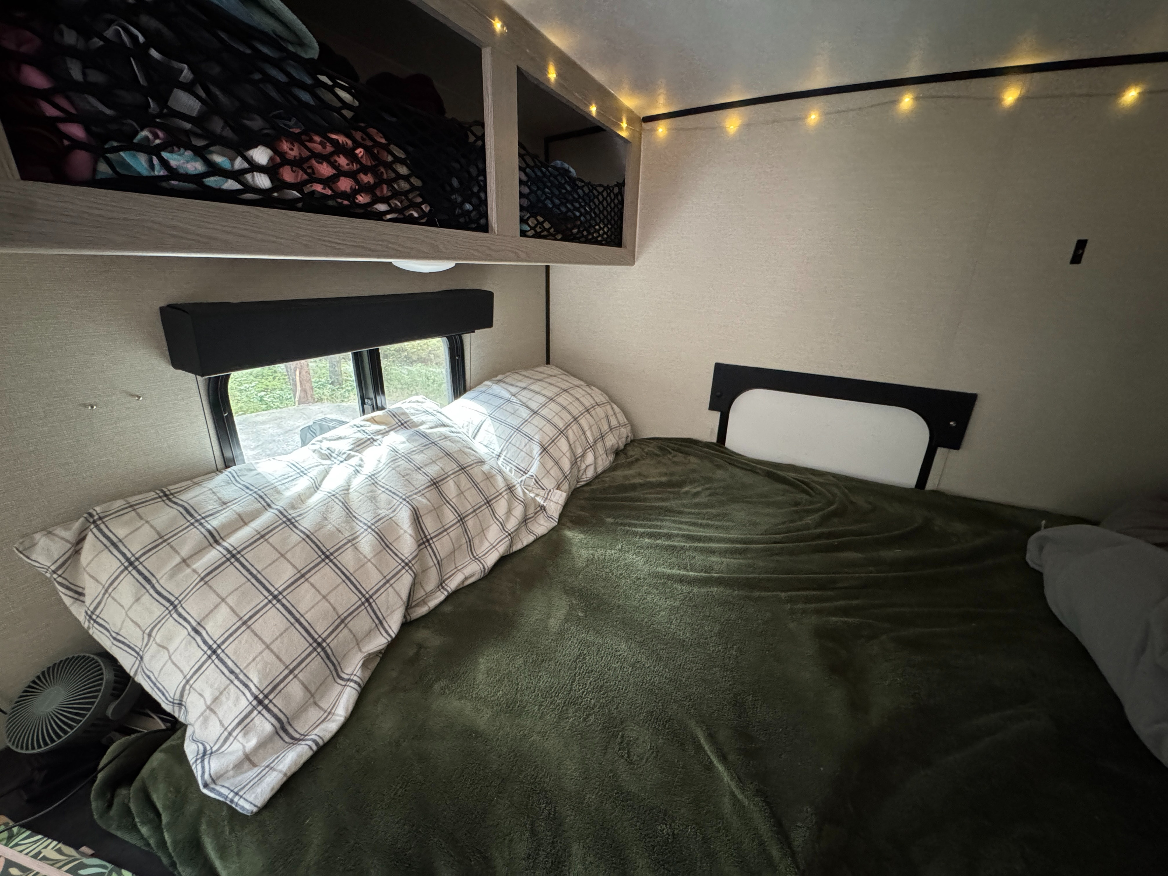Cozy RV rental bedroom with plaid bedding, green blanket, storage nets, and string lights, perfect for camping.. Coachmen Apex Remote 16R 2023