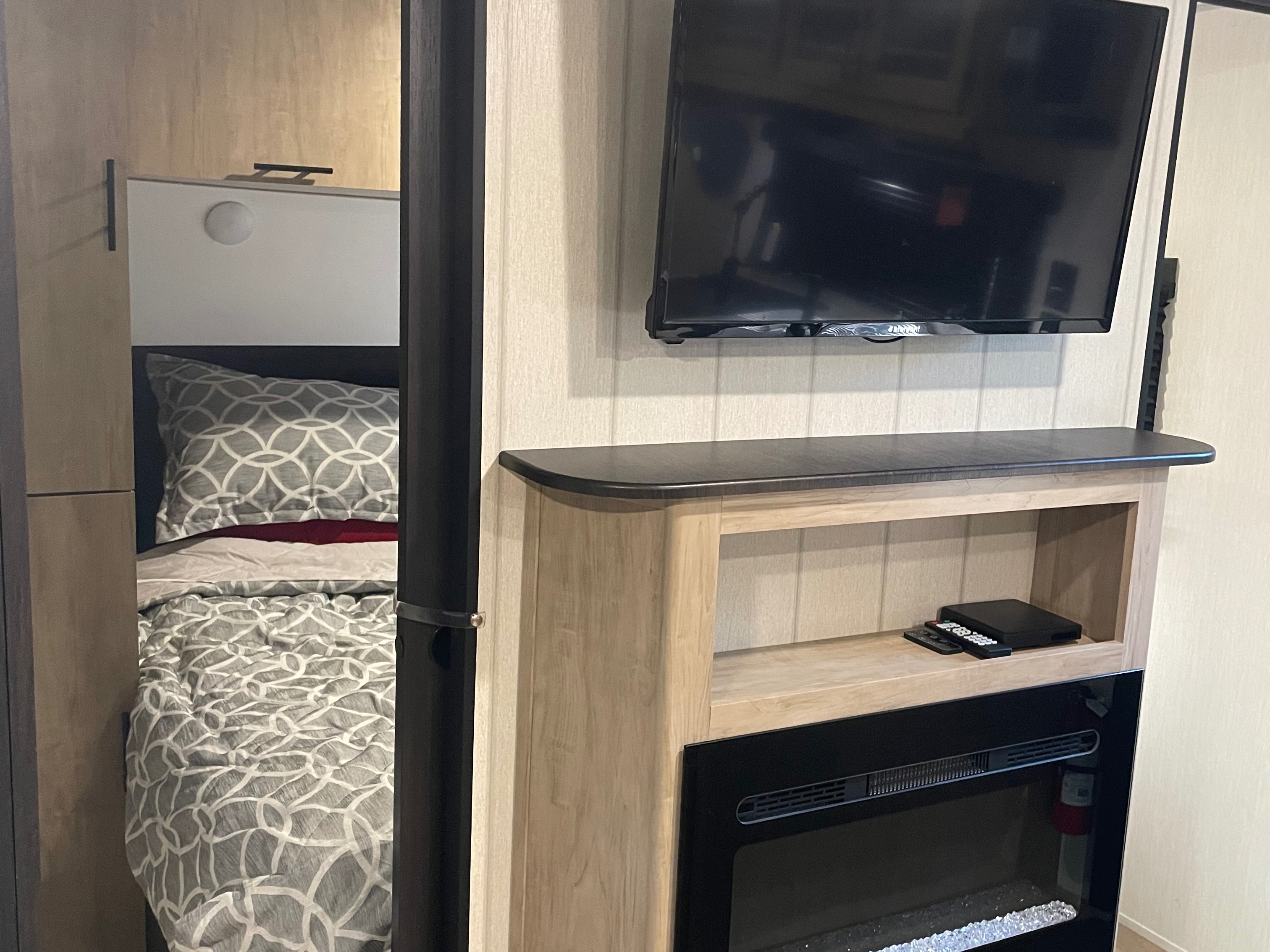 RV rental interior: bedroom area with bed & headboard light, facing a TV above an electric fireplace. Modern design.. Forest River Cherokee Grey Wolf 2026