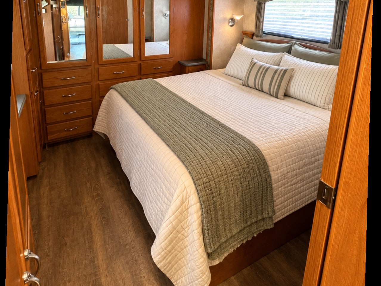 Cozy RV rental bedroom featuring a comfortable bed with striped pillows & quilted bedding, wooden cabinetry, and wood-look flooring.. Coachmen Aurora Select 2004