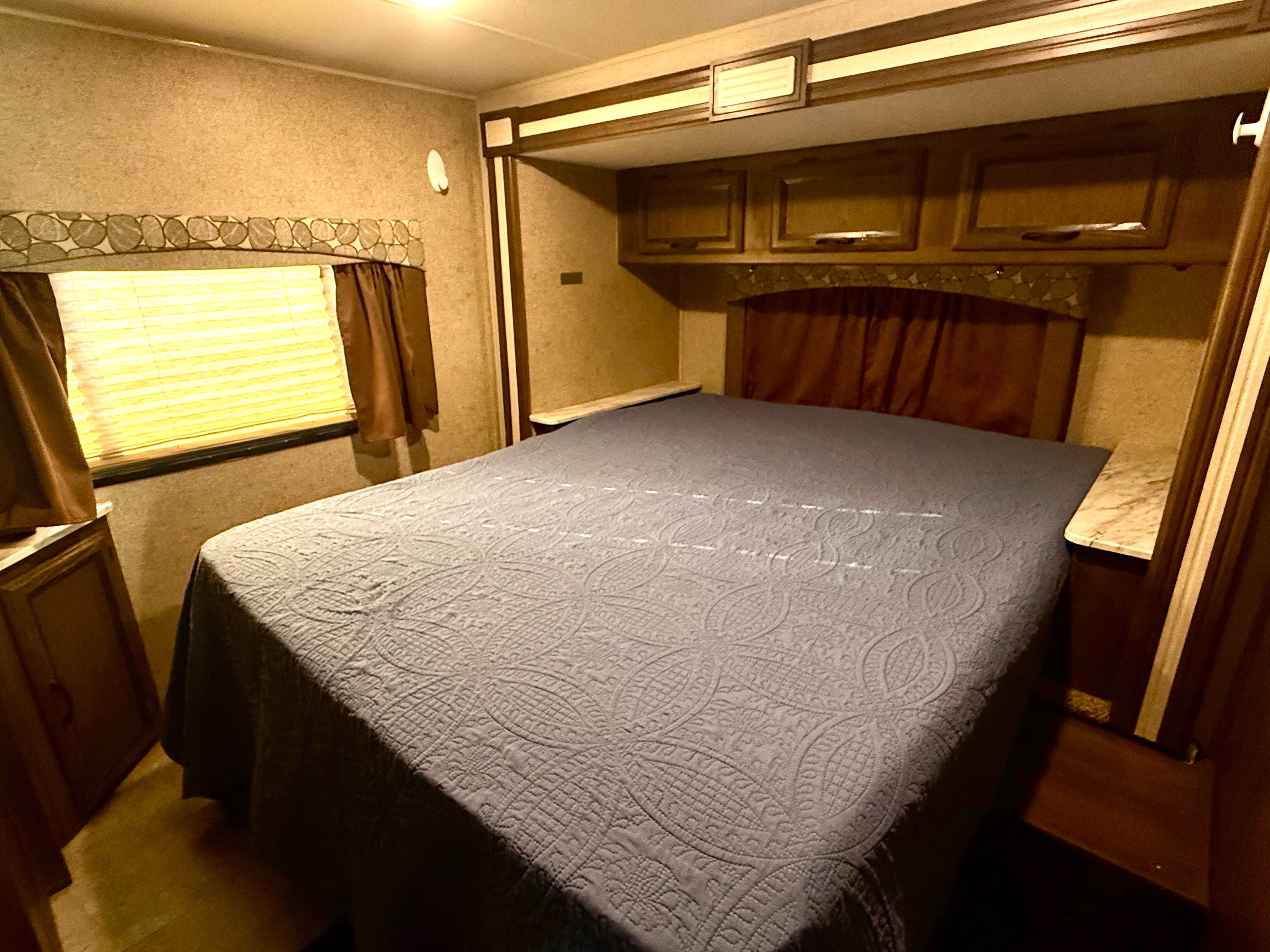 This cozy RV rental bedroom features a patterned bedspread, window with blinds, and built-in storage, perfect for travel.. Coachmen Freelander 26DS 2019