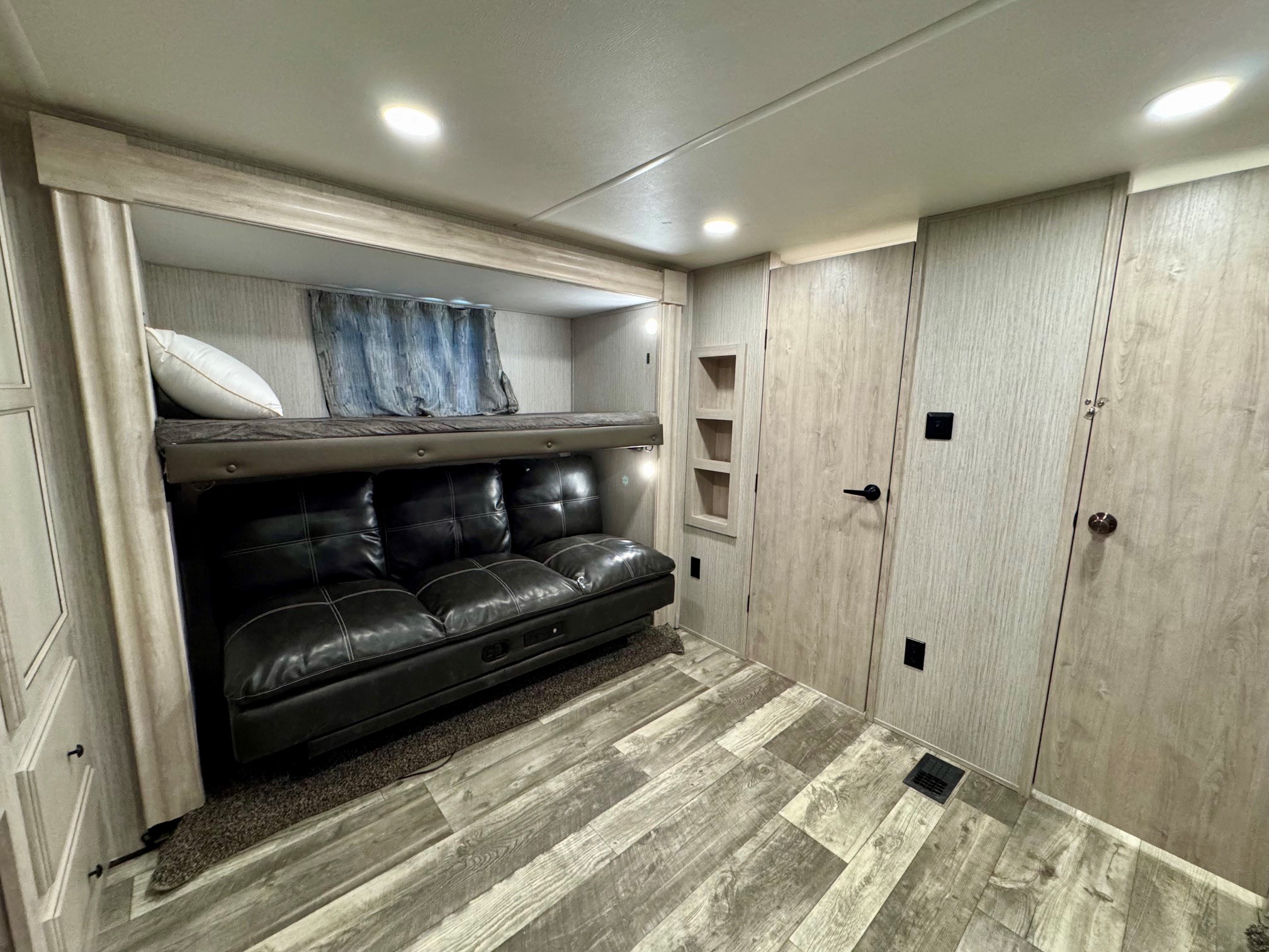 An RV rental's bunk room with a black sofa bed, upper bunk, light wood paneling, and wood-look flooring.. Forest River Sandpiper 2022