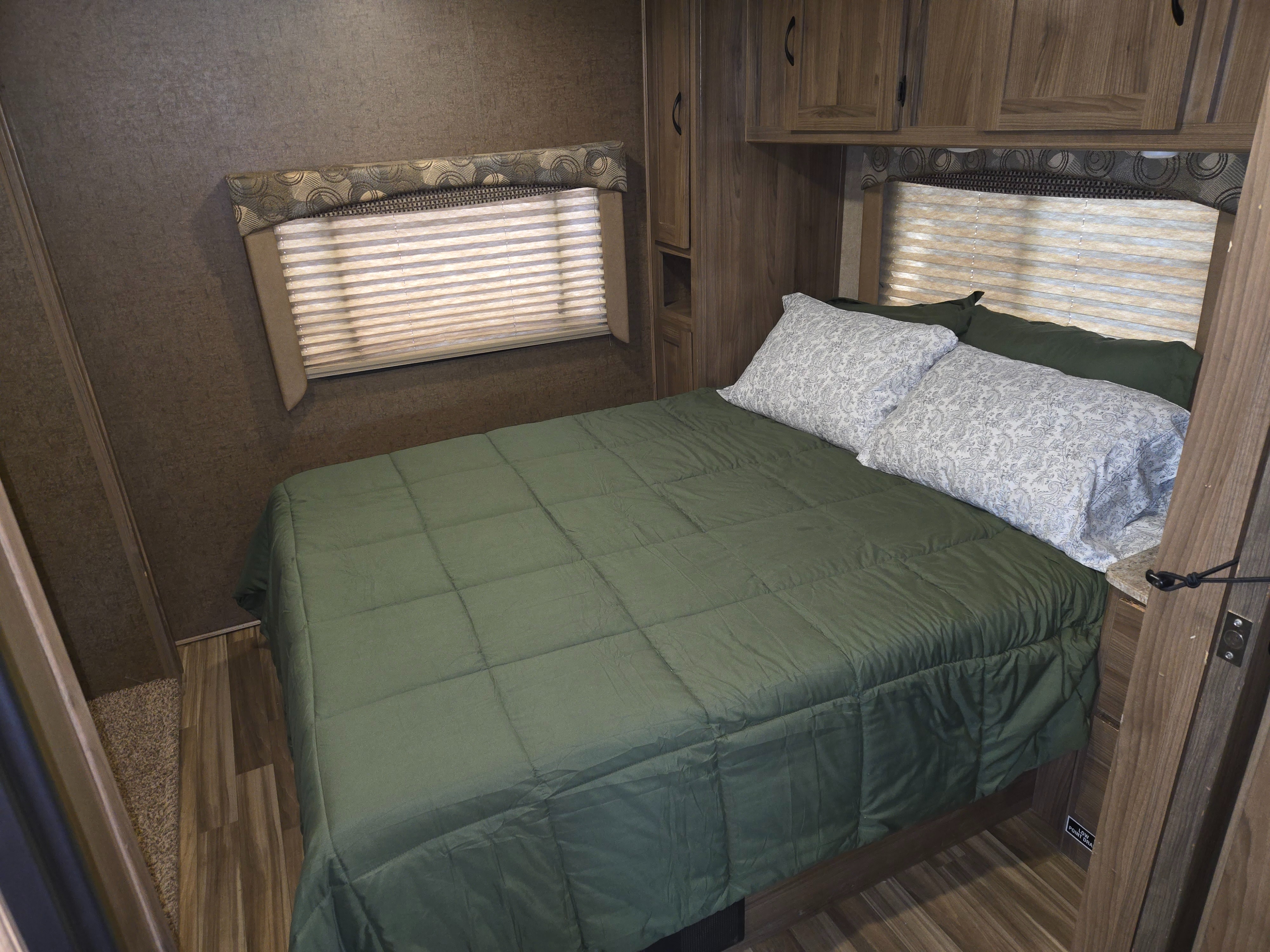 Cozy RV rental bedroom featuring a queen bed with a green comforter, patterned pillows, and practical wood-grain cabinetry.. Forest River Coachmen Freelander 2016