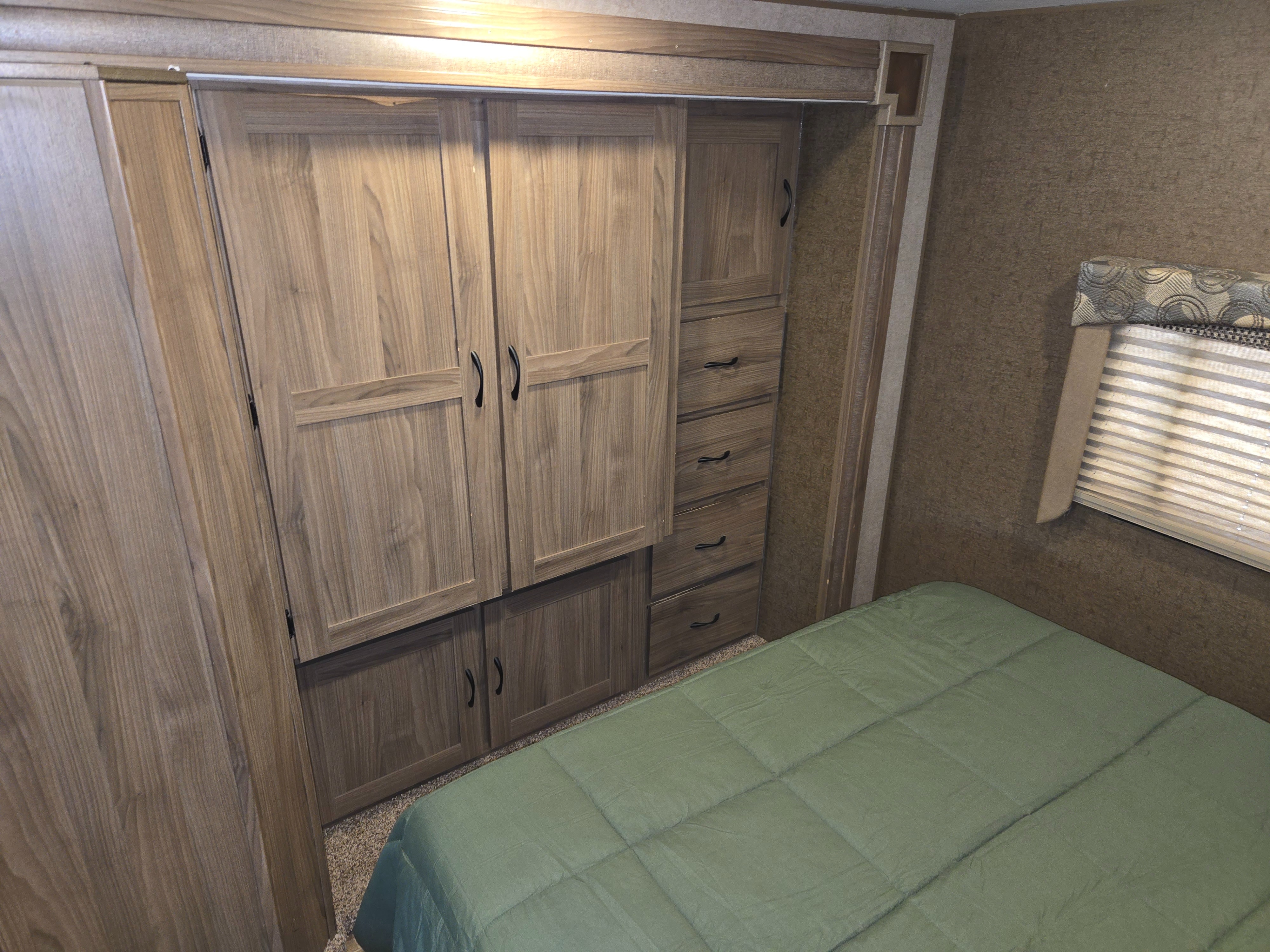 RV rental bedroom with a comfy bed, green comforter, and spacious wooden wardrobe with drawers for compact living.. Forest River Coachmen Freelander 2016